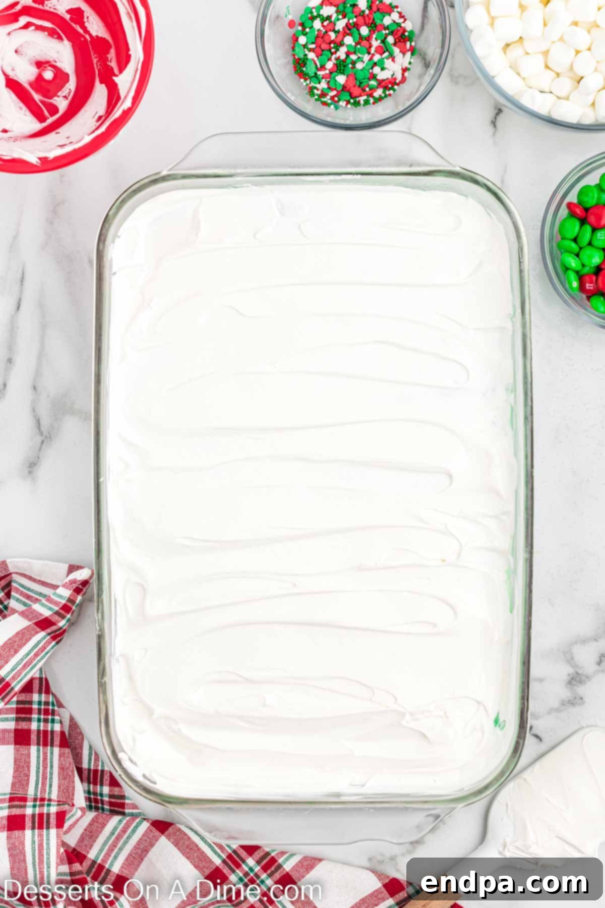 A smooth layer of cool whip spread over the green pudding layer in the dish.
