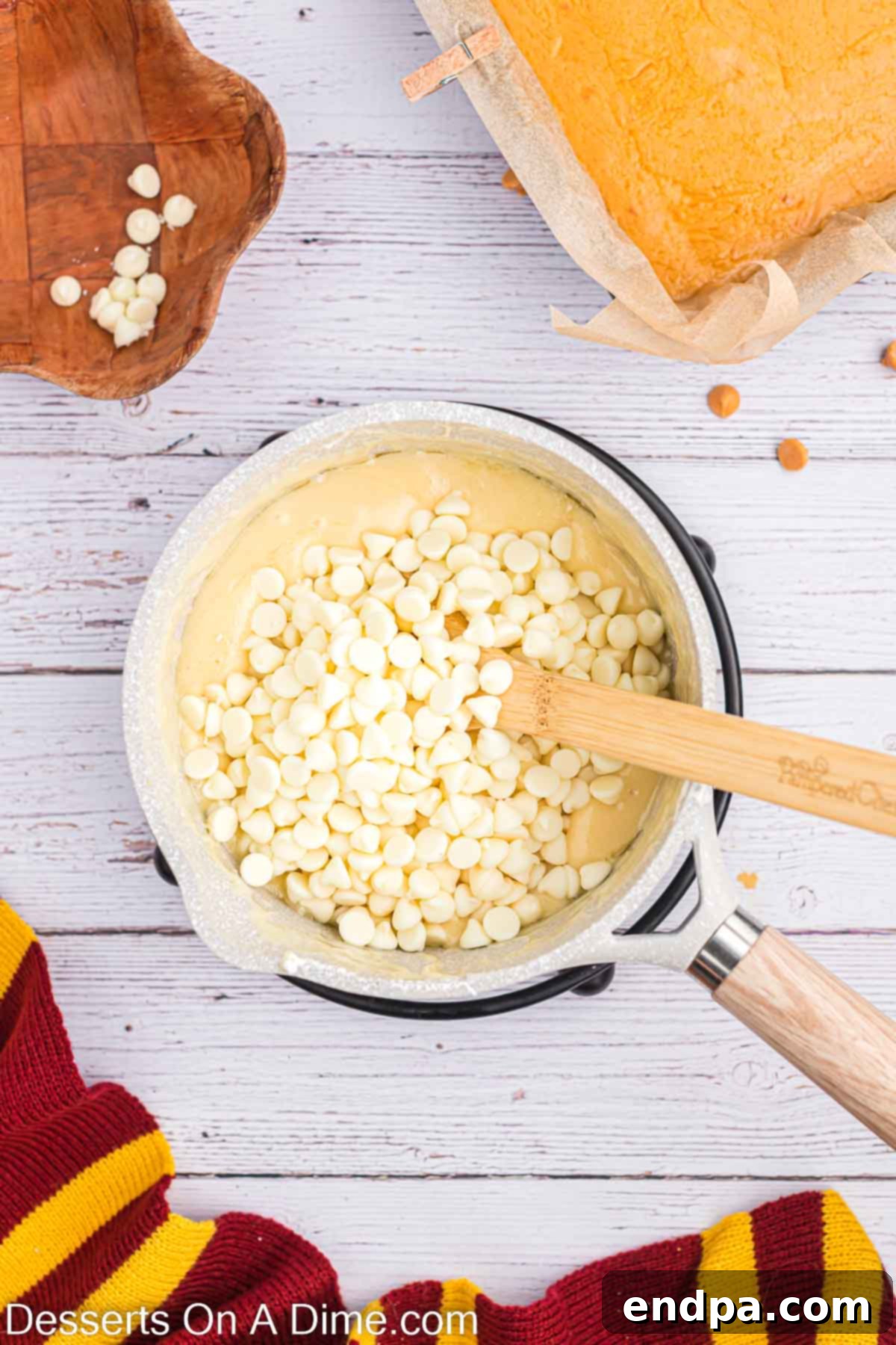 Dreamy Butterbeer Fudge 8 White chocolate chips being stirred into the hot vanilla mixture in a saucepan.