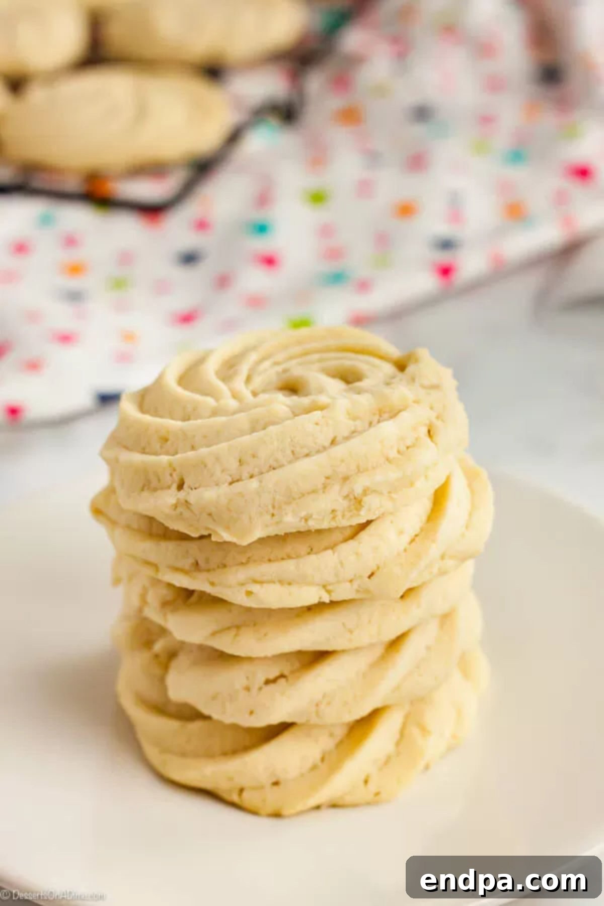 With just a few ingredients, Butter Cookies Recipe comes together quickly for a tasty and gorgeous treat. Easy butter cookies are so pretty and delicious. A stack of golden-brown butter cookies perfectly arranged on a white ceramic plate, showcasing their delicate and uniform appearance.
