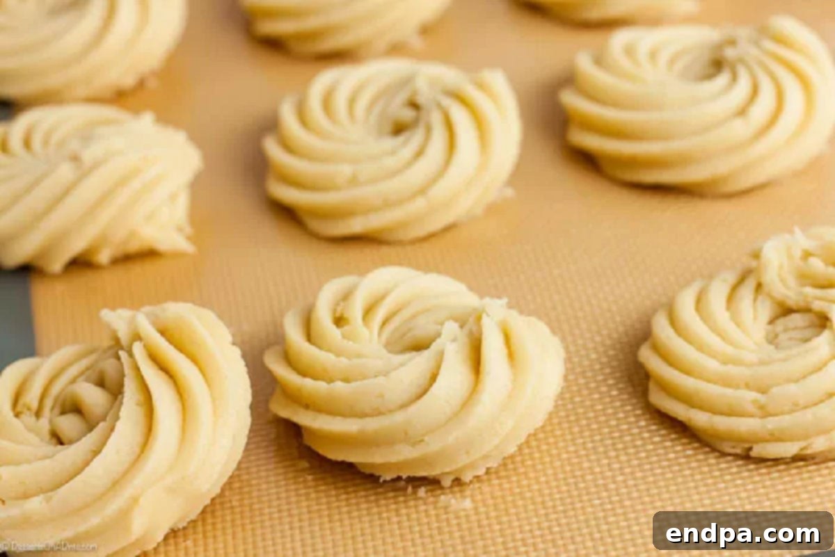 Perfectly Buttery Bites 3 Delicately piped cookie dough arranged in intricate patterns on a baking sheet, ready to be baked into beautiful butter cookies.