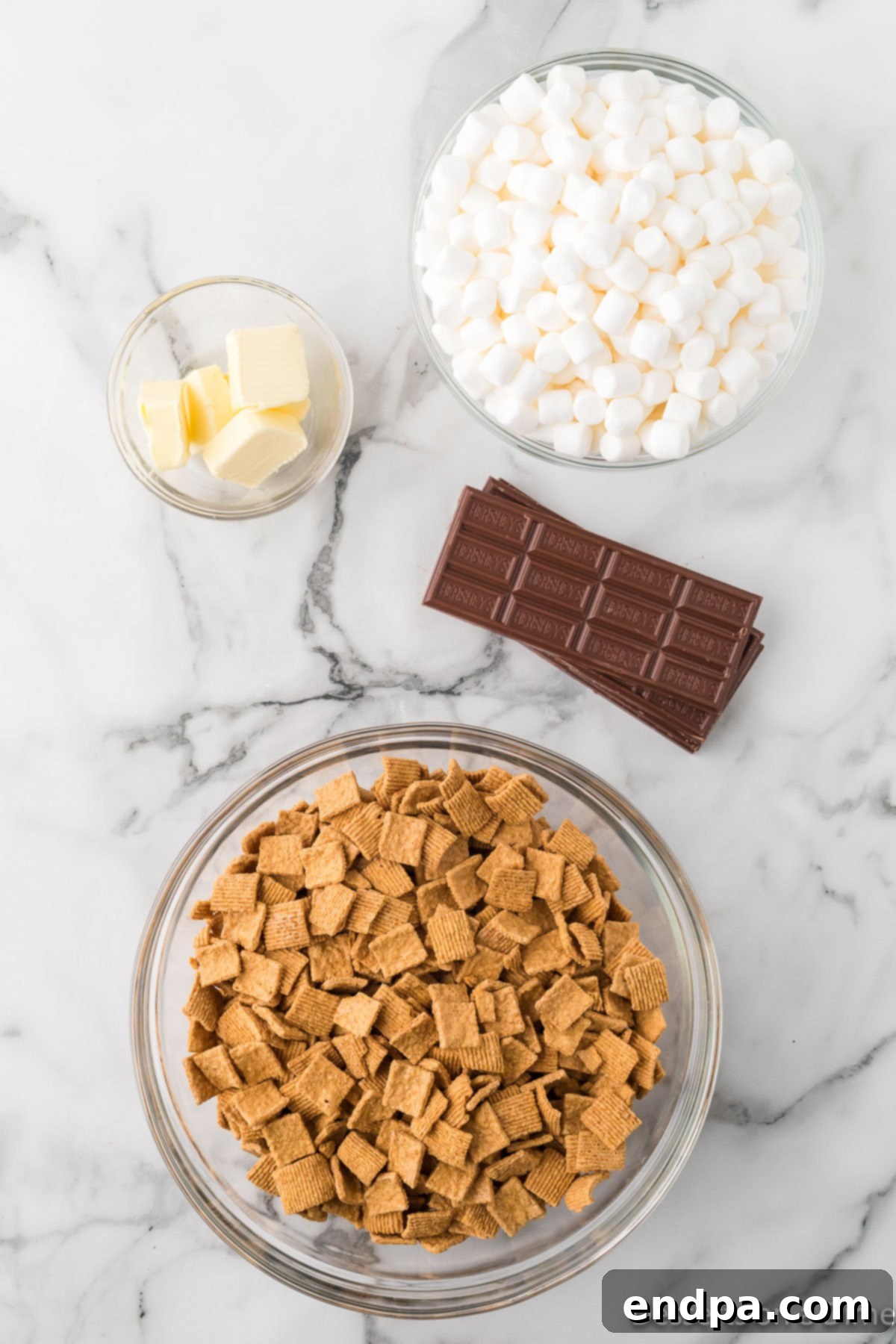 Ingredients for Golden Graham S'mores Bars laid out: butter, marshmallows, chocolate bars, and Golden Grahams cereal.