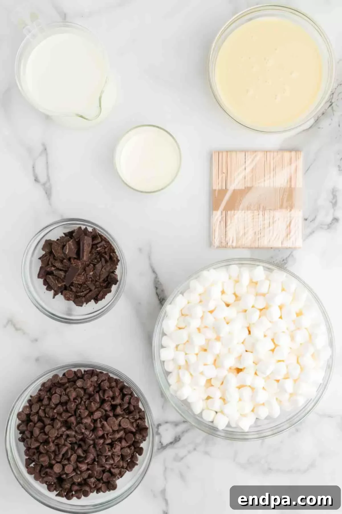 Ingredients for Hot Chocolate on a Stick laid out on a table, including chocolate chips, unsweetened chocolate, sweetened condensed milk, heavy cream, and mini marshmallows.