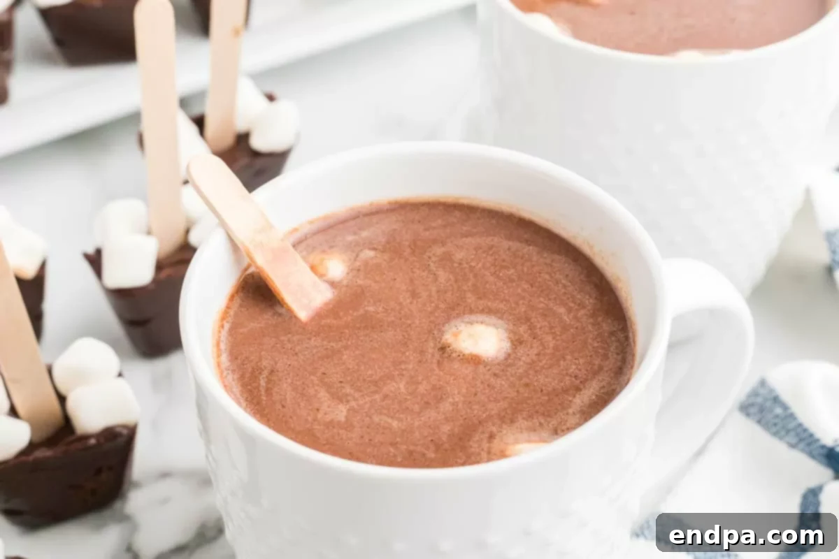 A single mug of hot cocoa with a hot chocolate stick, garnished with a candy cane.