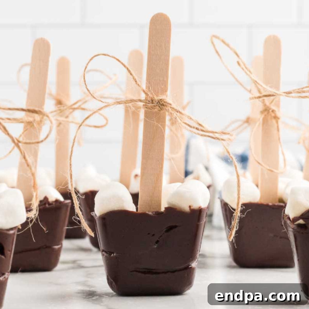 Two hot chocolate on a stick, one with a candy cane, in mugs ready to be enjoyed.