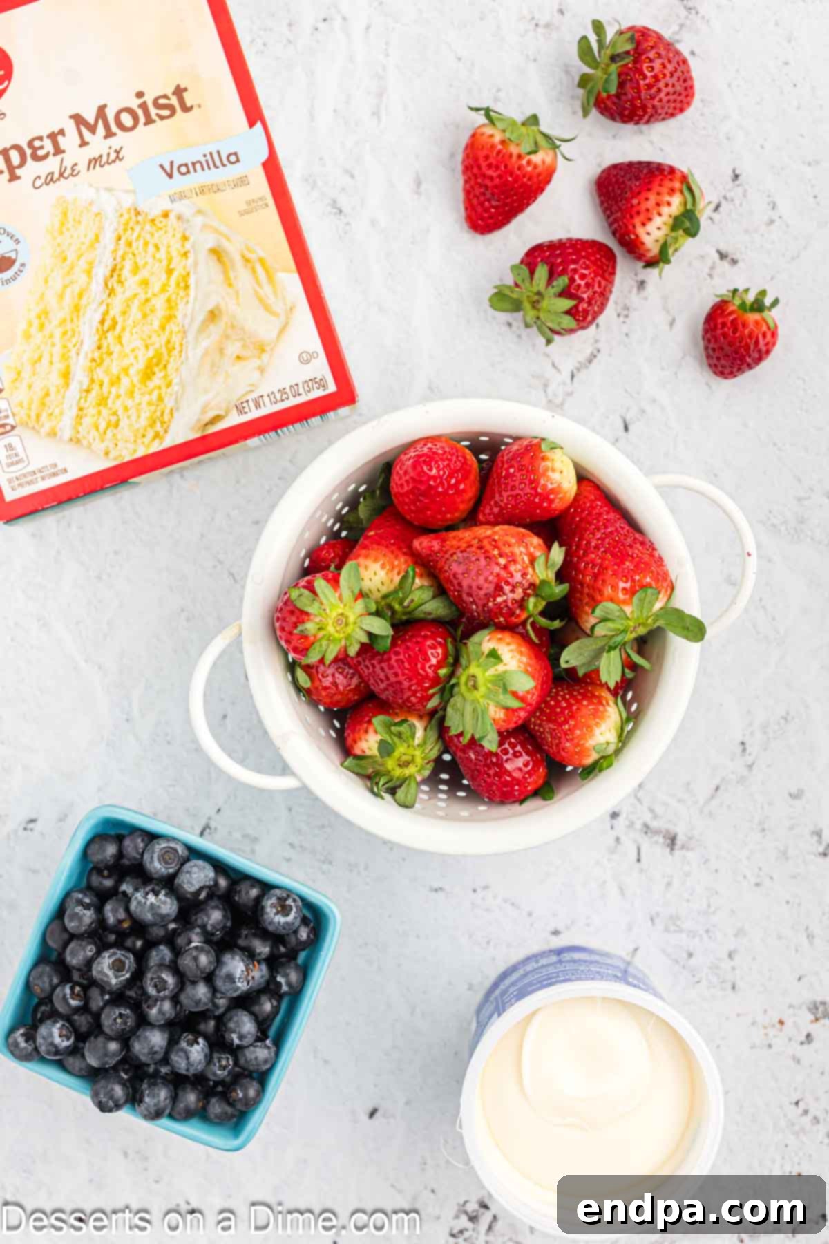 Ingredients for American Flag Cake including vanilla cake mix, vanilla icing, fresh blueberries, and sliced strawberries.