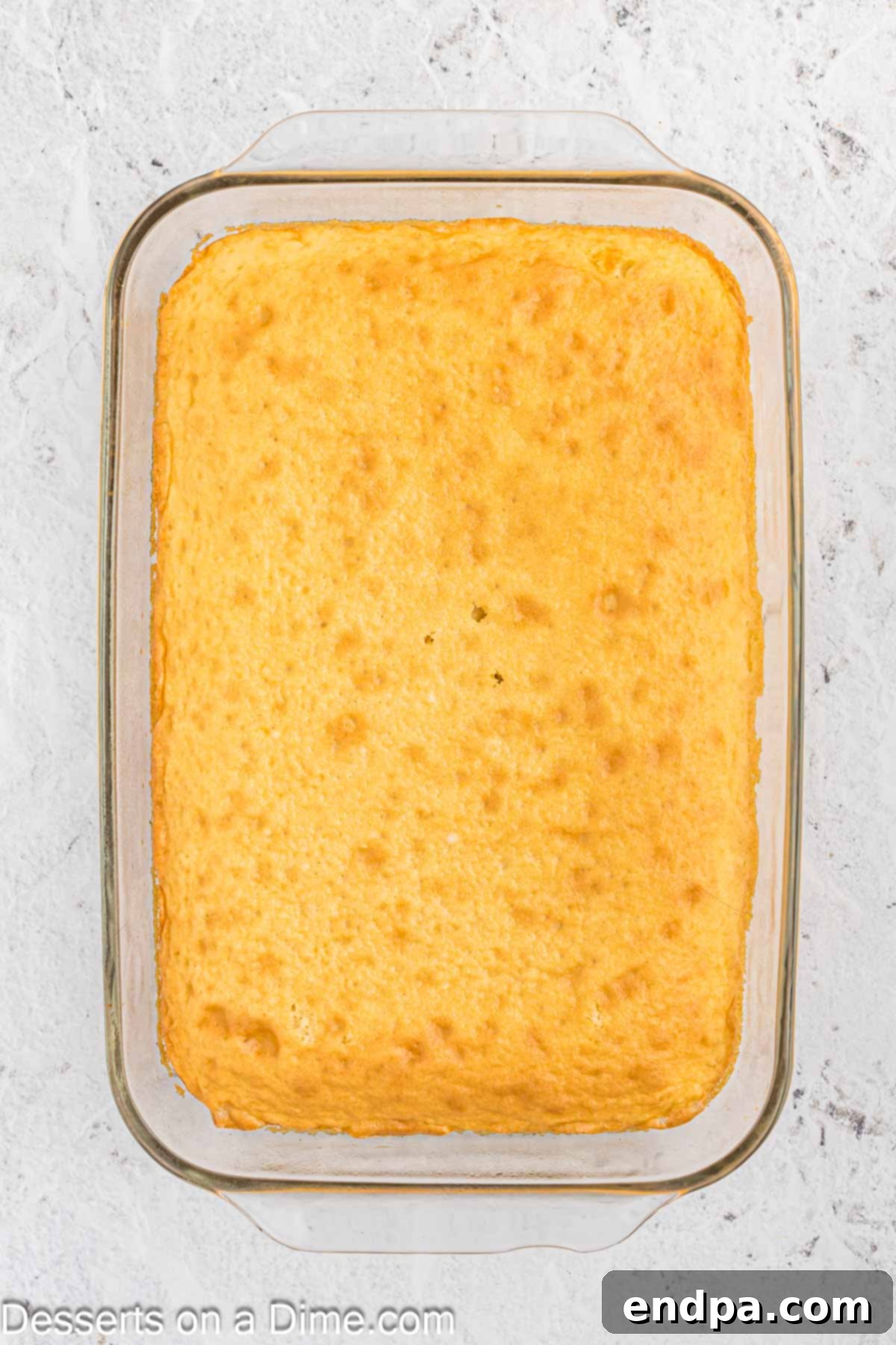 A baked vanilla cake cooling in a 9x13 inch pan on a wire rack.