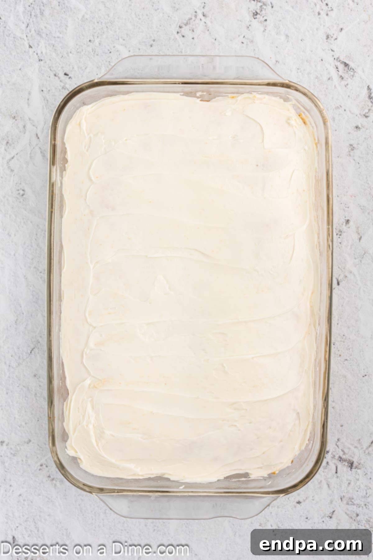 Vanilla icing being spread smoothly over a cooled sheet cake.
