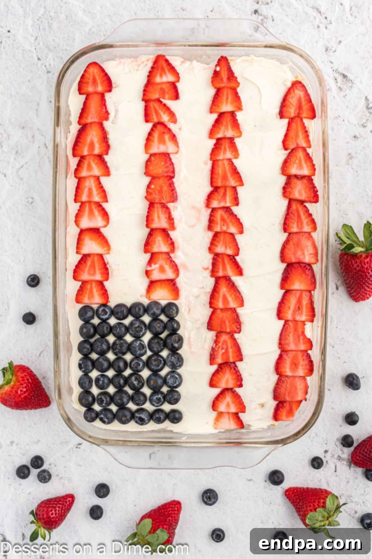 An American Flag Cake fully decorated with blueberries and rows of sliced strawberries, resembling the US flag.