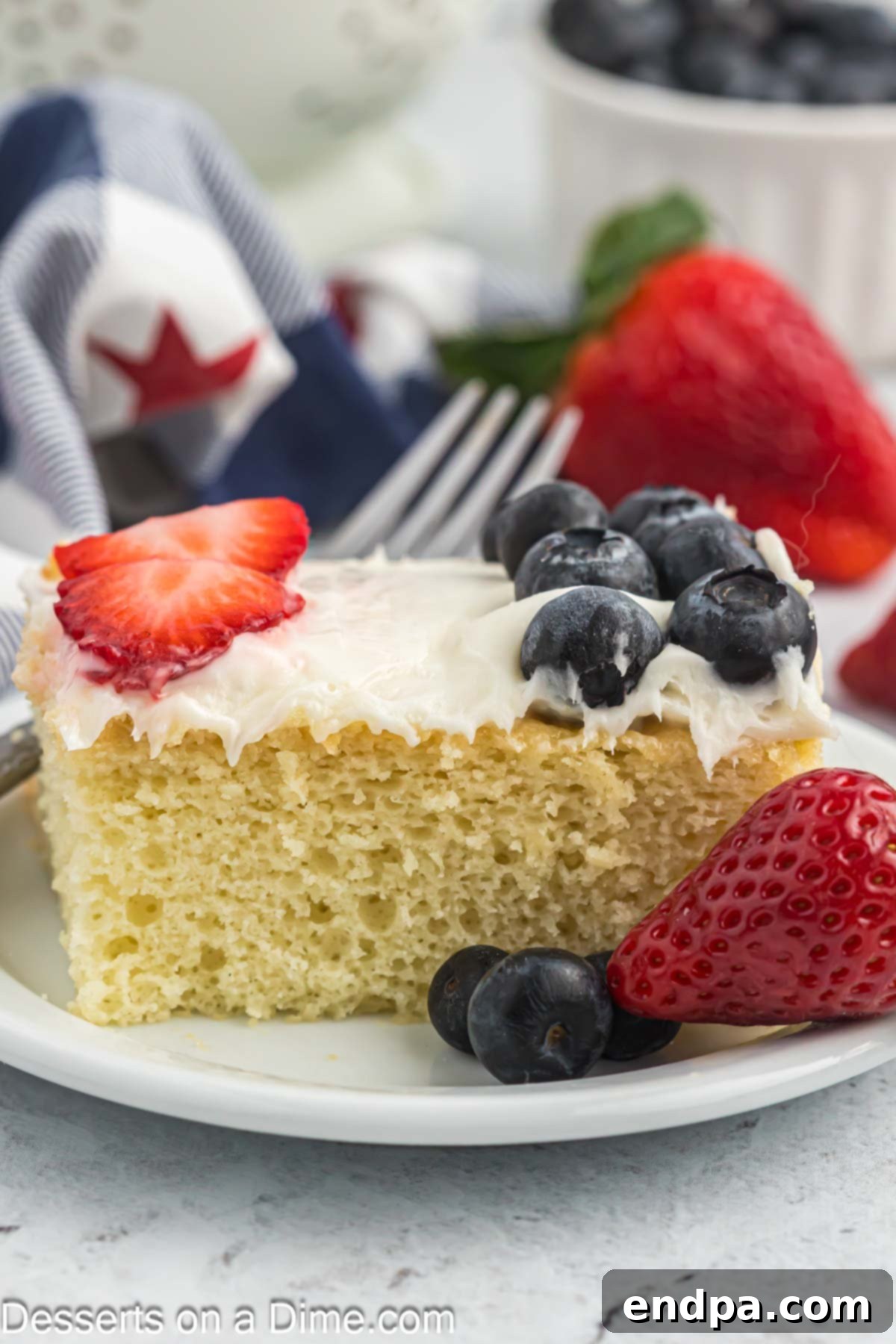 A slice of American Flag Cake, showing layers of cake, frosting, and berries, served on a plate.