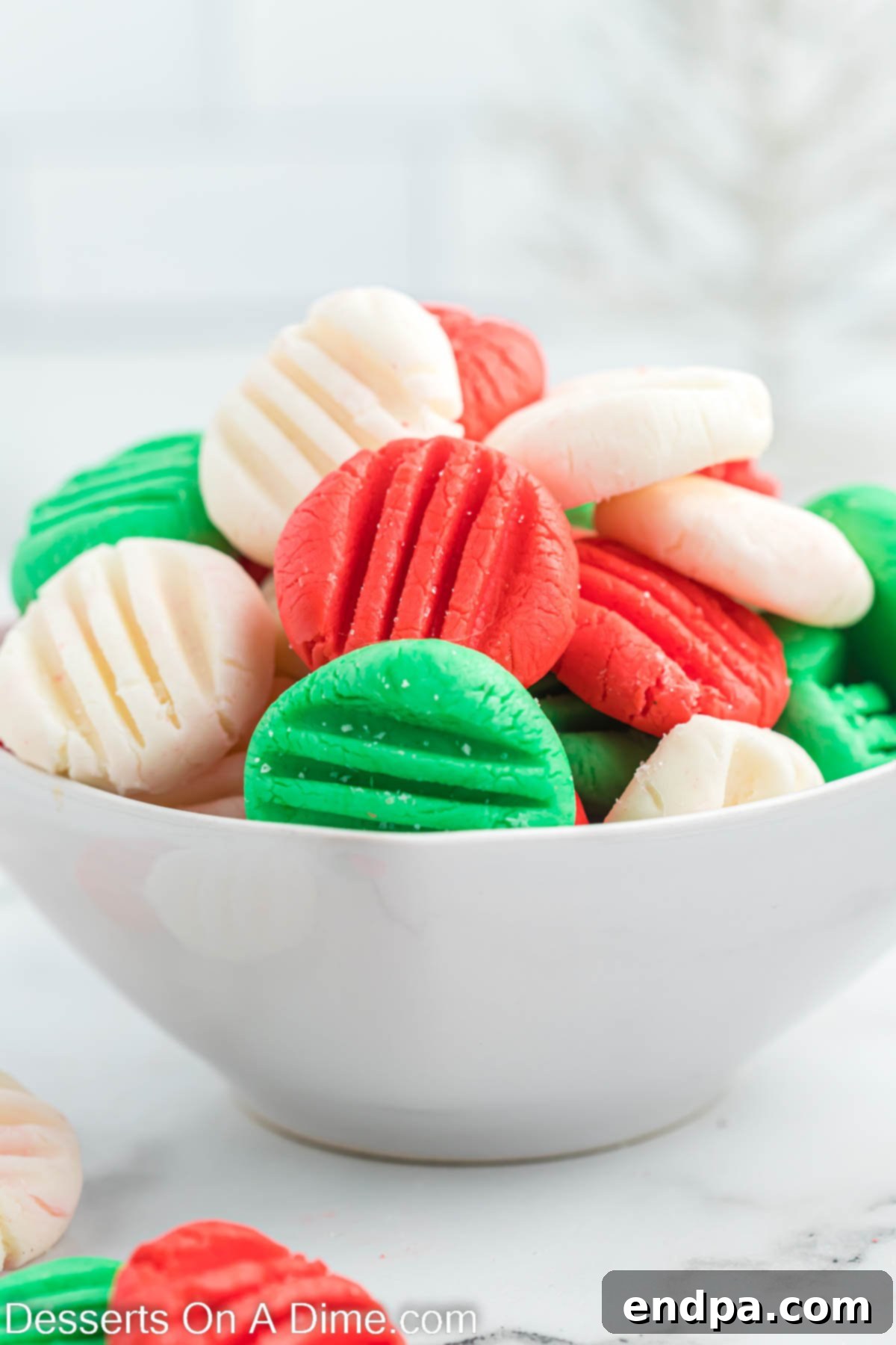 A bowl filled with vibrant red, green, and white Christmas mints, perfectly pressed with a fork design.