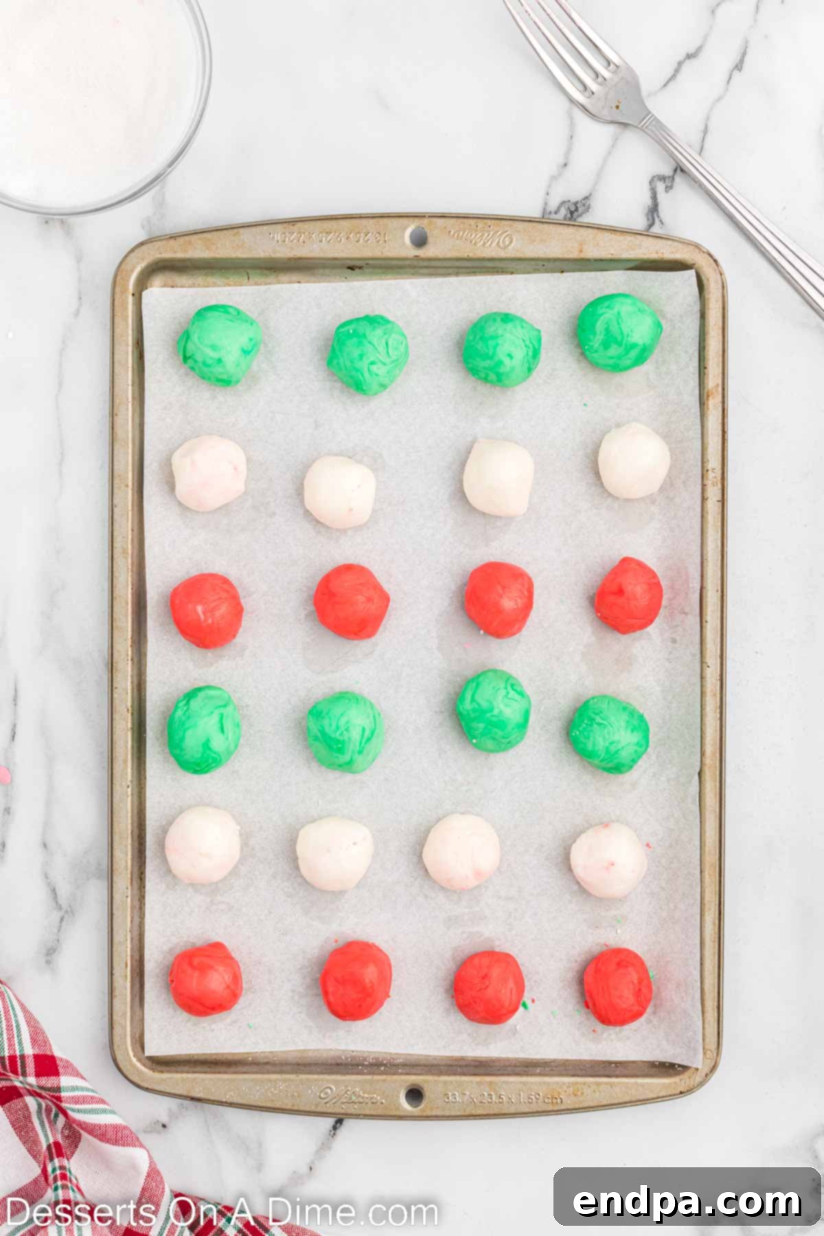 Small balls of colored mint dough are rolled and placed on a baking sheet lined with parchment paper.