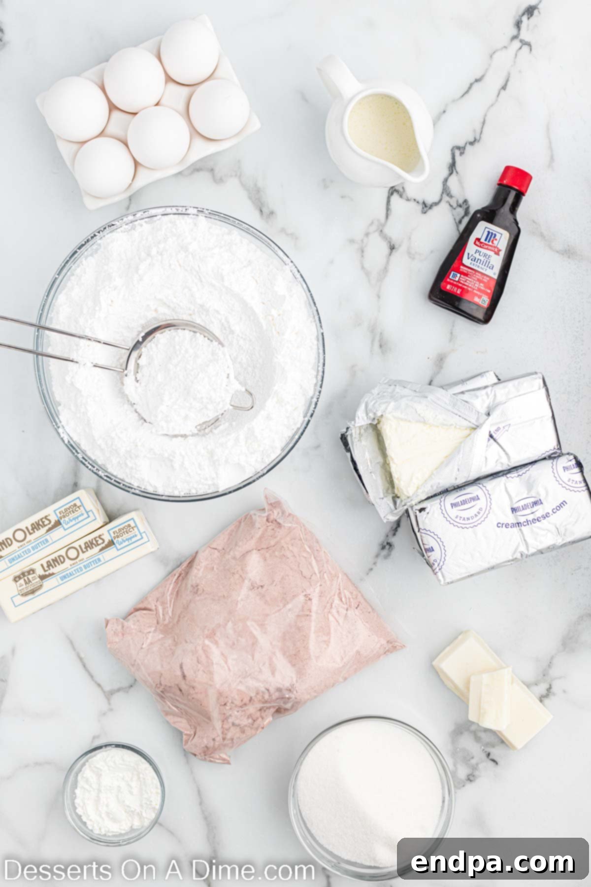 A beautiful flat lay of all the essential ingredients: red velvet cake mix, blocks of cream cheese, sugar, cornstarch, eggs, vanilla extract, heavy whipping cream, powdered sugar, and butter.