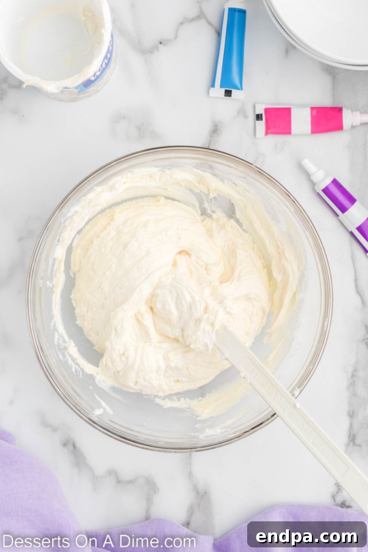 Enchanted Unicorn Swirl Fudge 5 A mixing bowl showing white frosting being stirred into melted white chocolate, creating a smooth mixture.