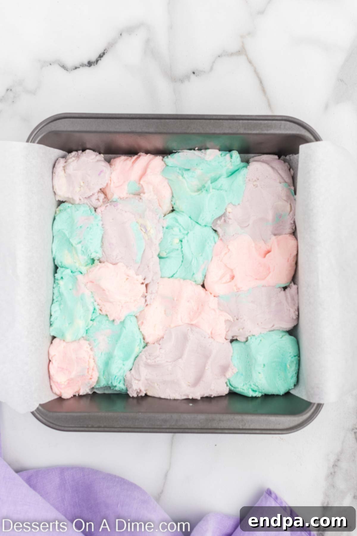 Enchanted Unicorn Swirl Fudge 7 The prepared 8x8 inch baking pan, with spoonfuls of pink, purple, and blue fudge dolloped randomly across its surface.