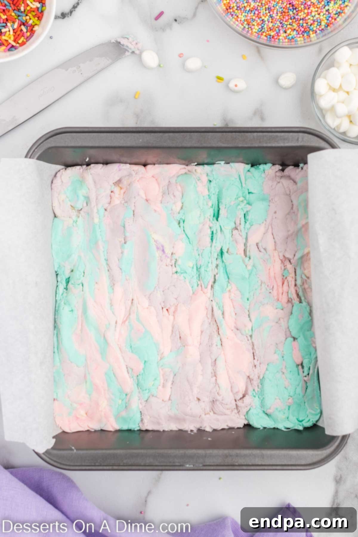 Enchanted Unicorn Swirl Fudge 8 A knife gently swirling through the dolloped colorful fudge in the pan, creating a marbled pattern.