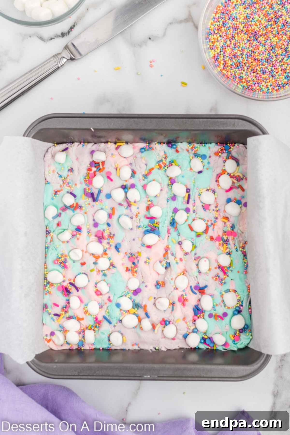 Enchanted Unicorn Swirl Fudge 9 The swirled unicorn fudge in the pan, generously topped with mini marshmallows and rainbow sprinkles, ready to be chilled.
