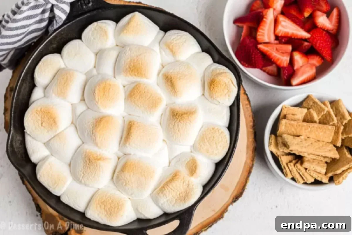 Smores dip in a cast iron skillet with a side of strawberries and graham crackers