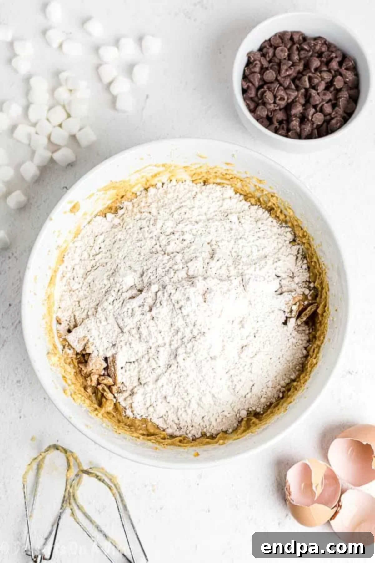 Campfire Smores Cookies 2 A mixing bowl containing all-purpose flour, coarsely crushed graham crackers, and baking powder, perfectly combined for the dry ingredients of the s'mores cookies.