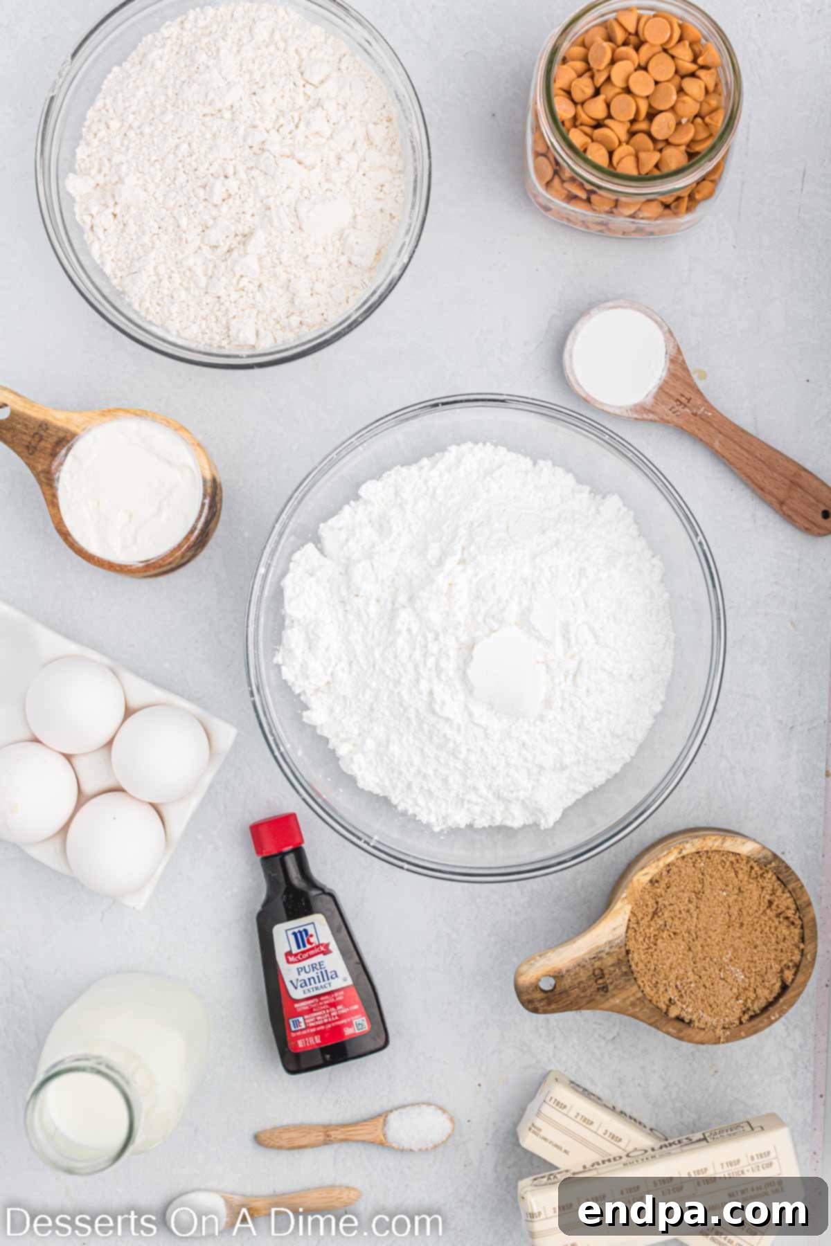 Butterscotch Bliss Cake 3 A collection of ingredients for homemade butterscotch cake including flour, baking soda, butter, dark brown sugar, vanilla extract, eggs, sour cream, butterscotch chips, and powdered sugar, arranged on a countertop.