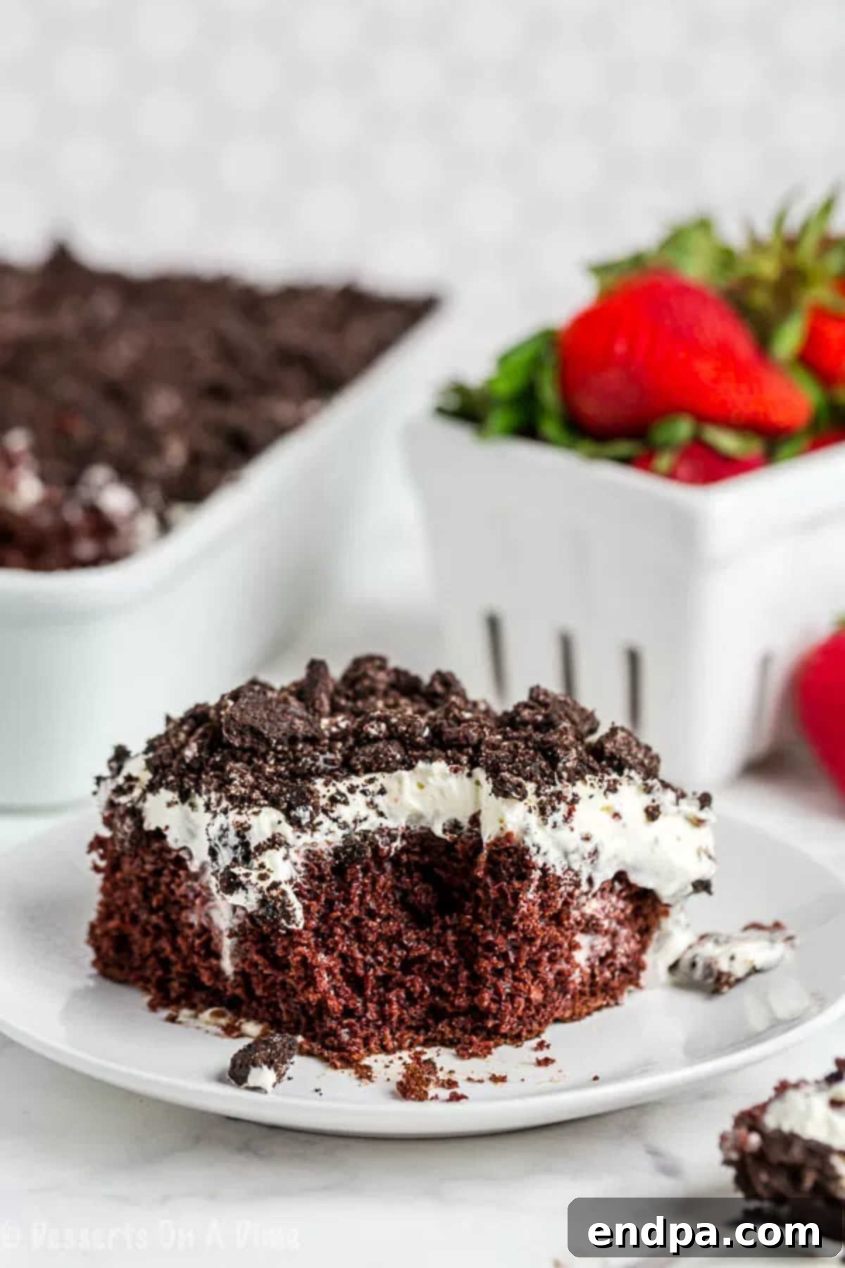Close up image of a slice of Oreo poke cake on a white plate, showcasing its layers.