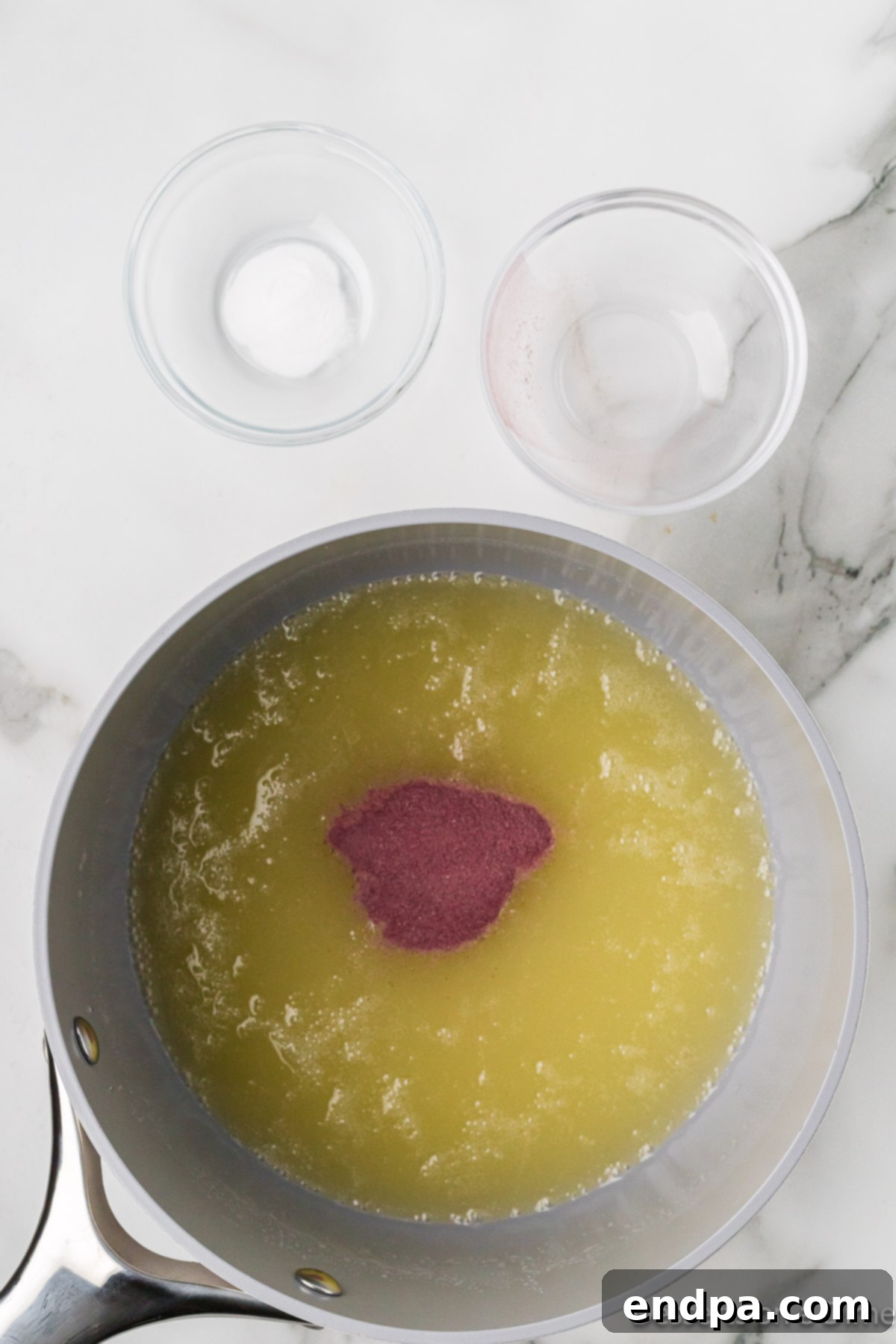 The vibrant Kool-Aid powder being stirred into the boiled syrup mixture in a saucepan.