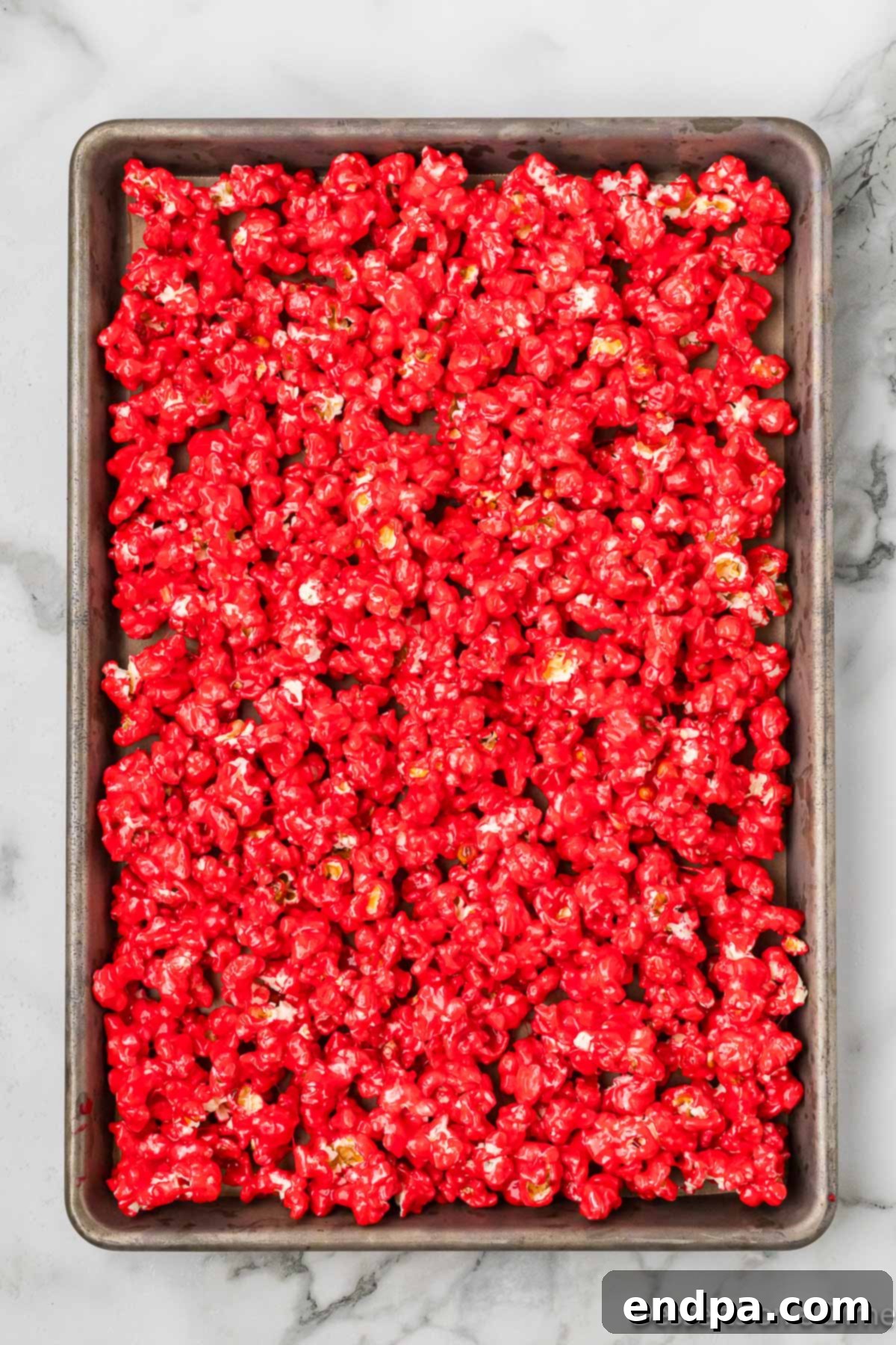 The coated Kool-Aid popcorn spread out in a single layer on a baking sheet, ready for the oven.