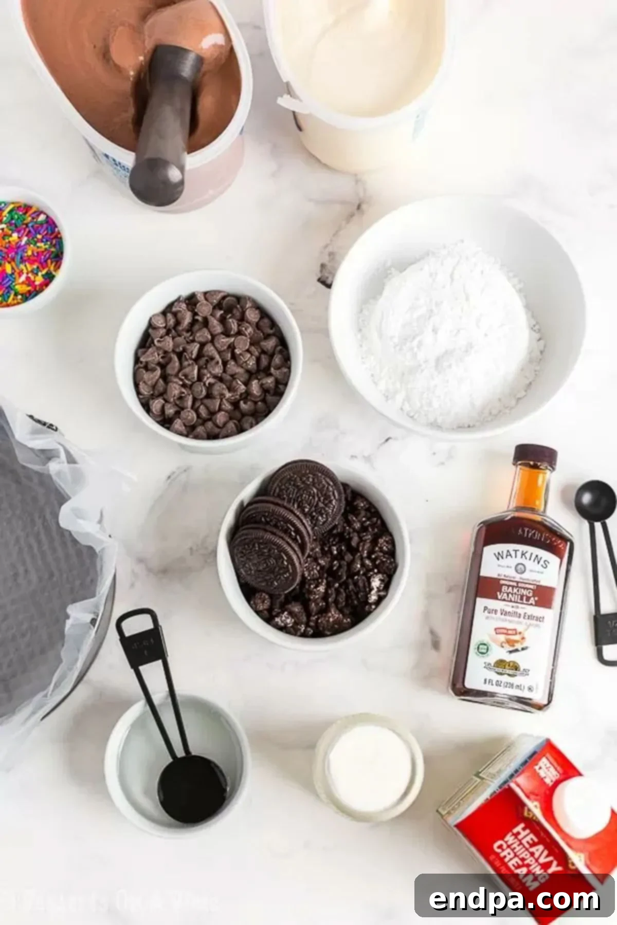 Gather Your Supplies: The Simple Ingredients for Dairy Queen Ice Cream Cake A vibrant display of all the necessary ingredients laid out: Oreo crumbs, creamy vanilla ice cream, rich chocolate ice cream, semi-sweet chocolate chips, corn syrup, pure vanilla extract, heavy whipping cream, powdered sugar, and colorful sprinkles.