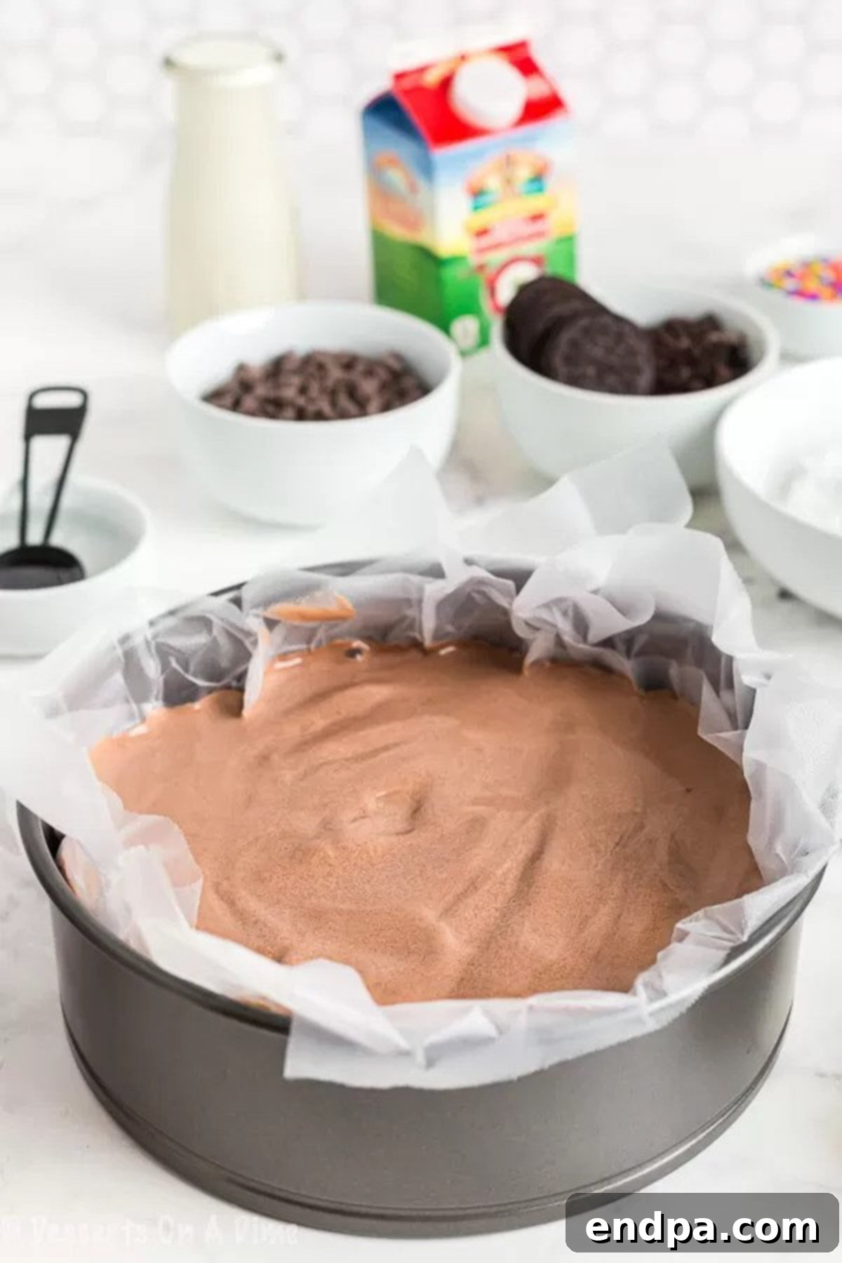The Ultimate Homemade Ice Cream Cake 5 A frozen chocolate ice cream layer in a springform pan, covered with a layer of clear plastic wrap, ready for the next step.
