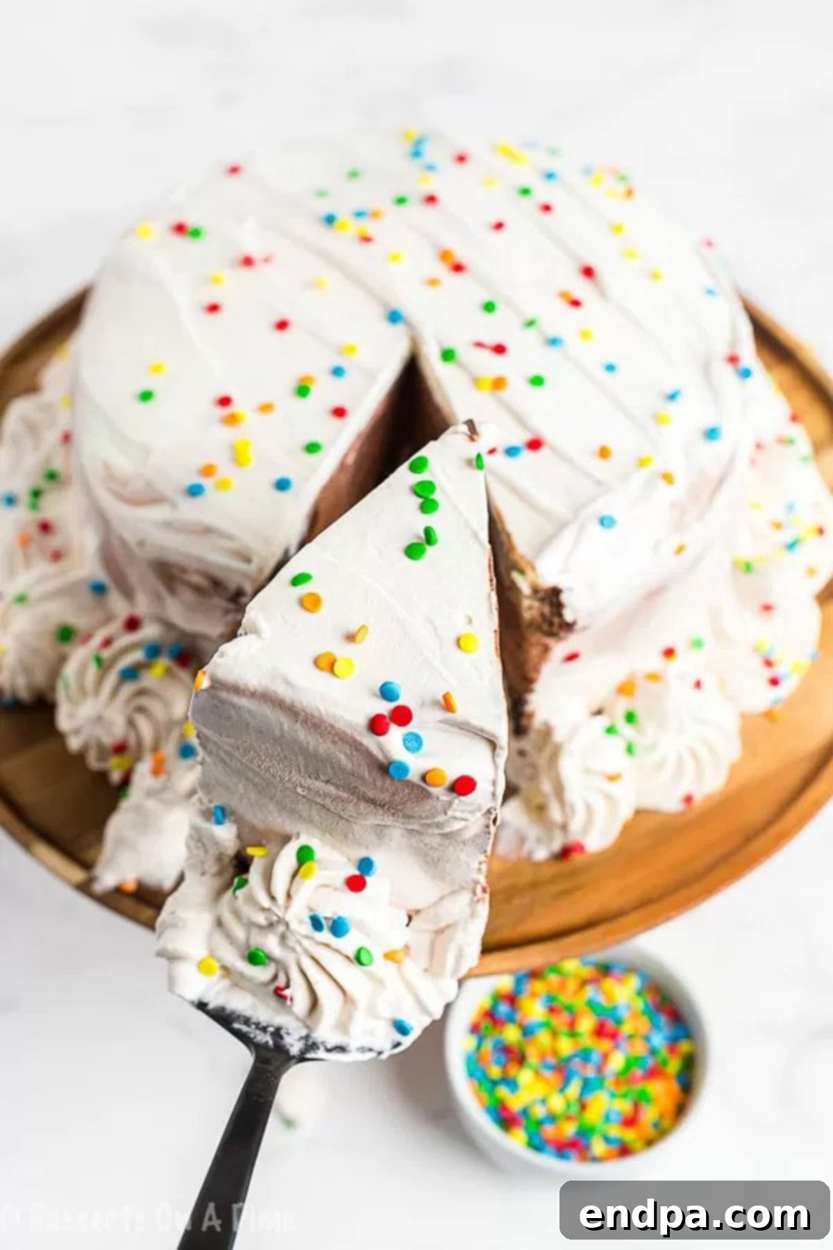 The Ultimate Homemade Ice Cream Cake 7 A pristine white ice cream cake with one slice removed, showcasing its perfect layers, on a cake pan.