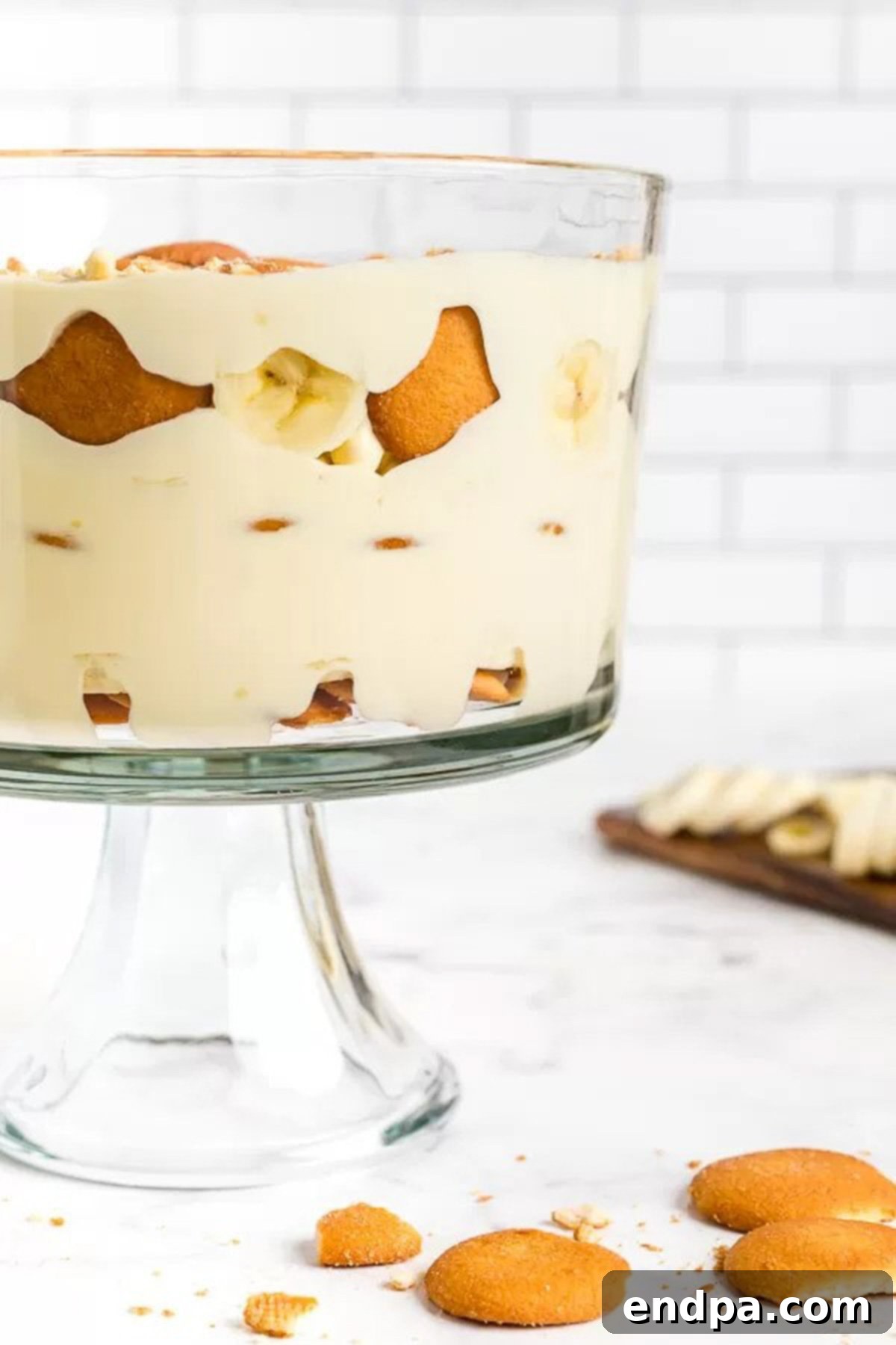 Close-up image of a beautifully layered banana pudding in a glass trifle dish, garnished with Nilla wafers.