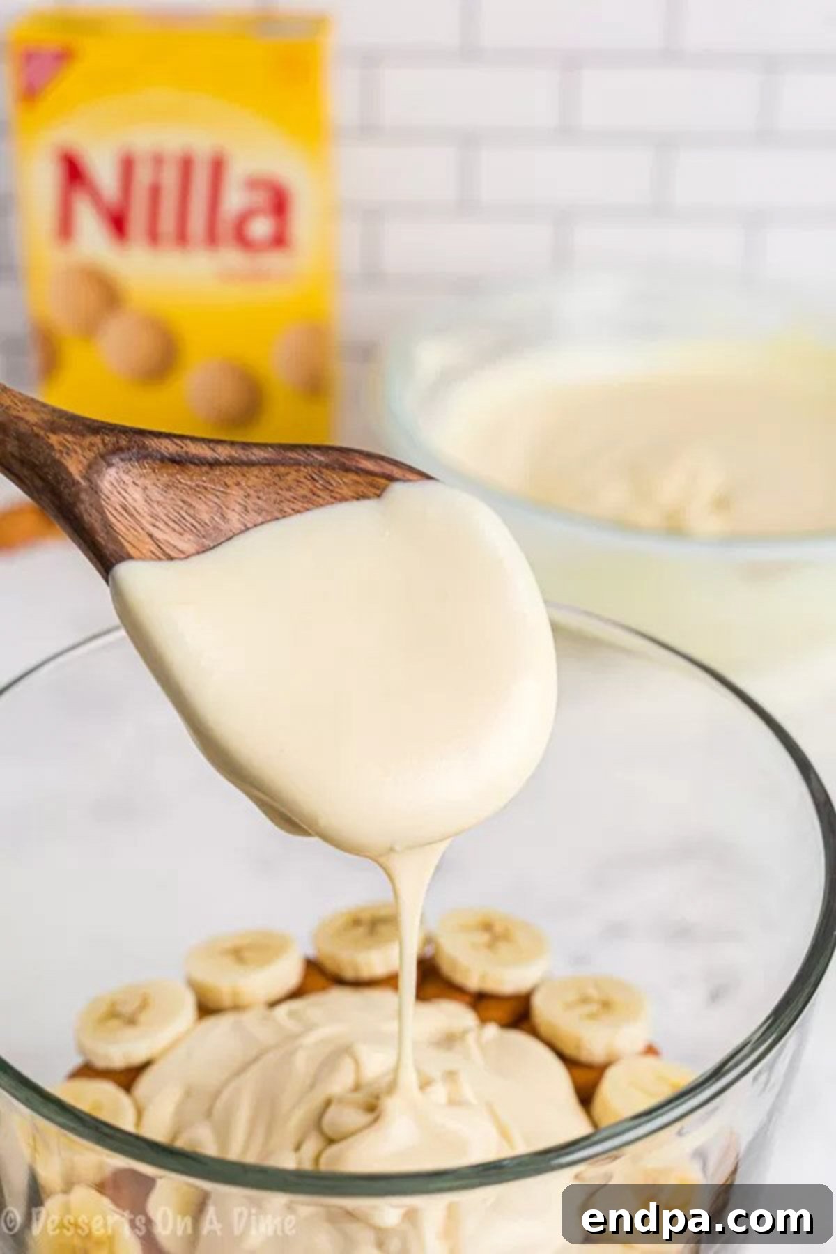 Close-up image of the first layers of Nilla wafers, bananas, and pudding mixture being carefully arranged in a clear glass trifle dish.