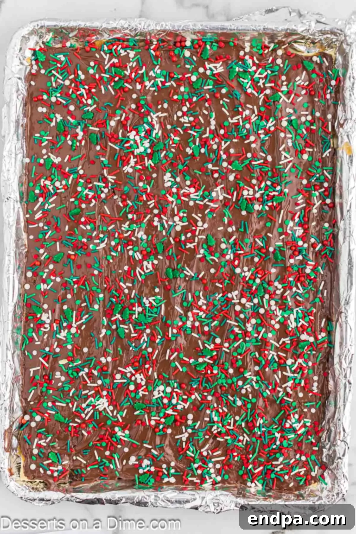 A close-up shot of vibrant Christmas sprinkles scattered over the warm, melted chocolate layer on the saltine toffee, adding a festive touch.