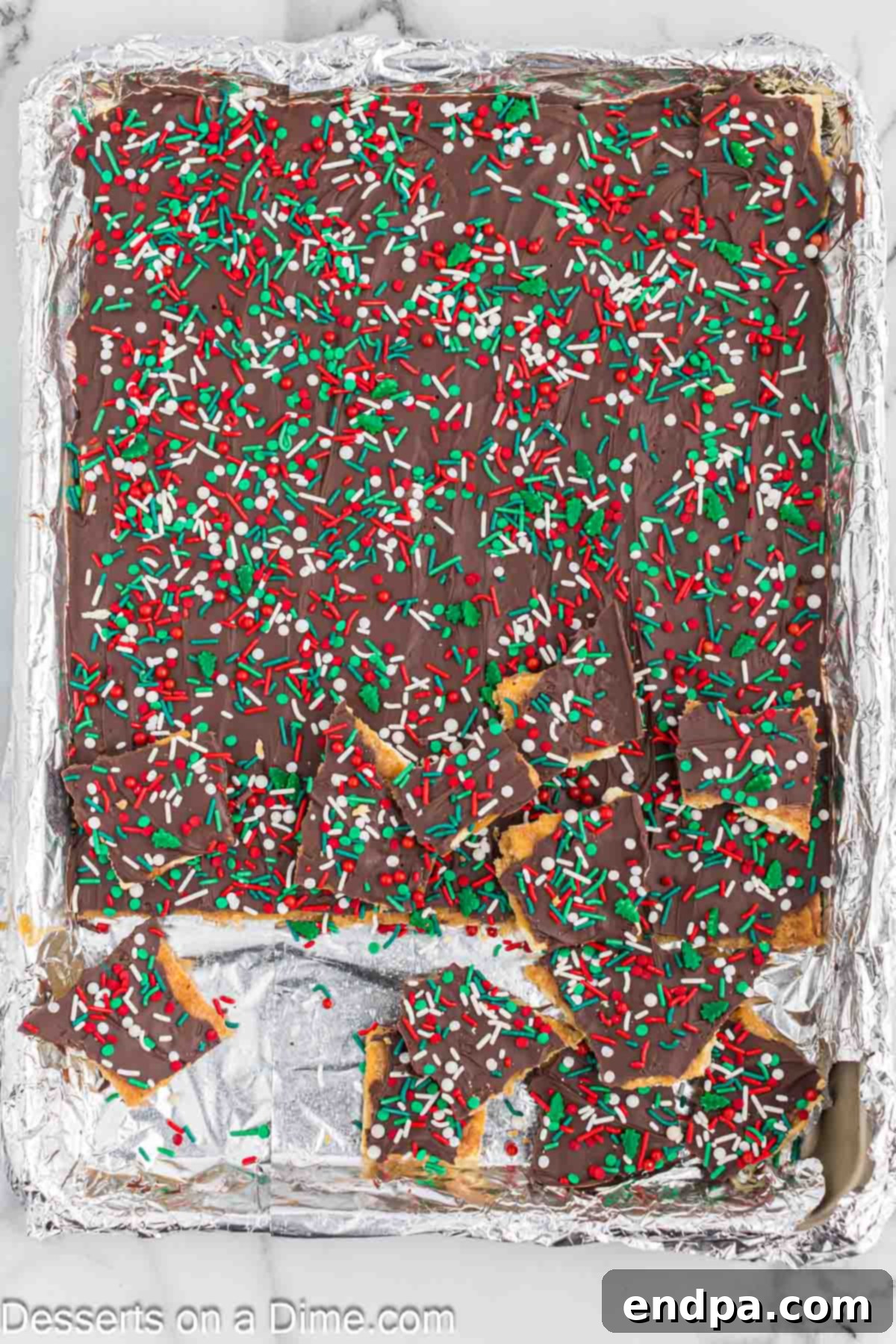 The fully assembled Christmas Crack, with its chocolate and sprinkle topping, cooling and hardening in the refrigerator on a baking sheet.