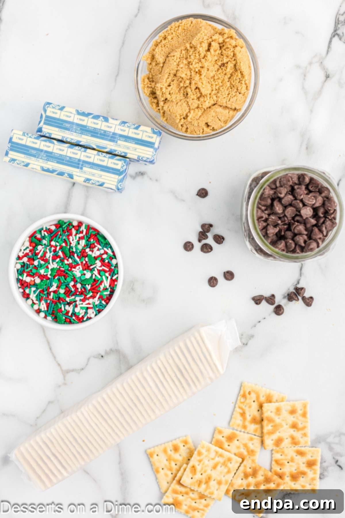 Arrangement of key Christmas Crack ingredients: saltine crackers, rich butter, brown sugar, semi-sweet chocolate chips, and colorful Christmas sprinkles.