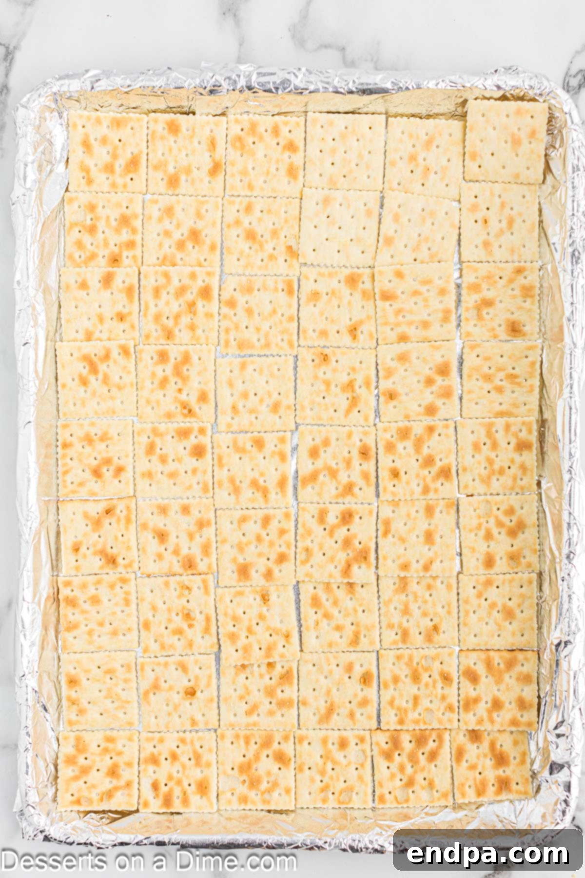 Saltine crackers carefully arranged in a single layer on a foil-lined baking sheet, ready for the toffee topping.