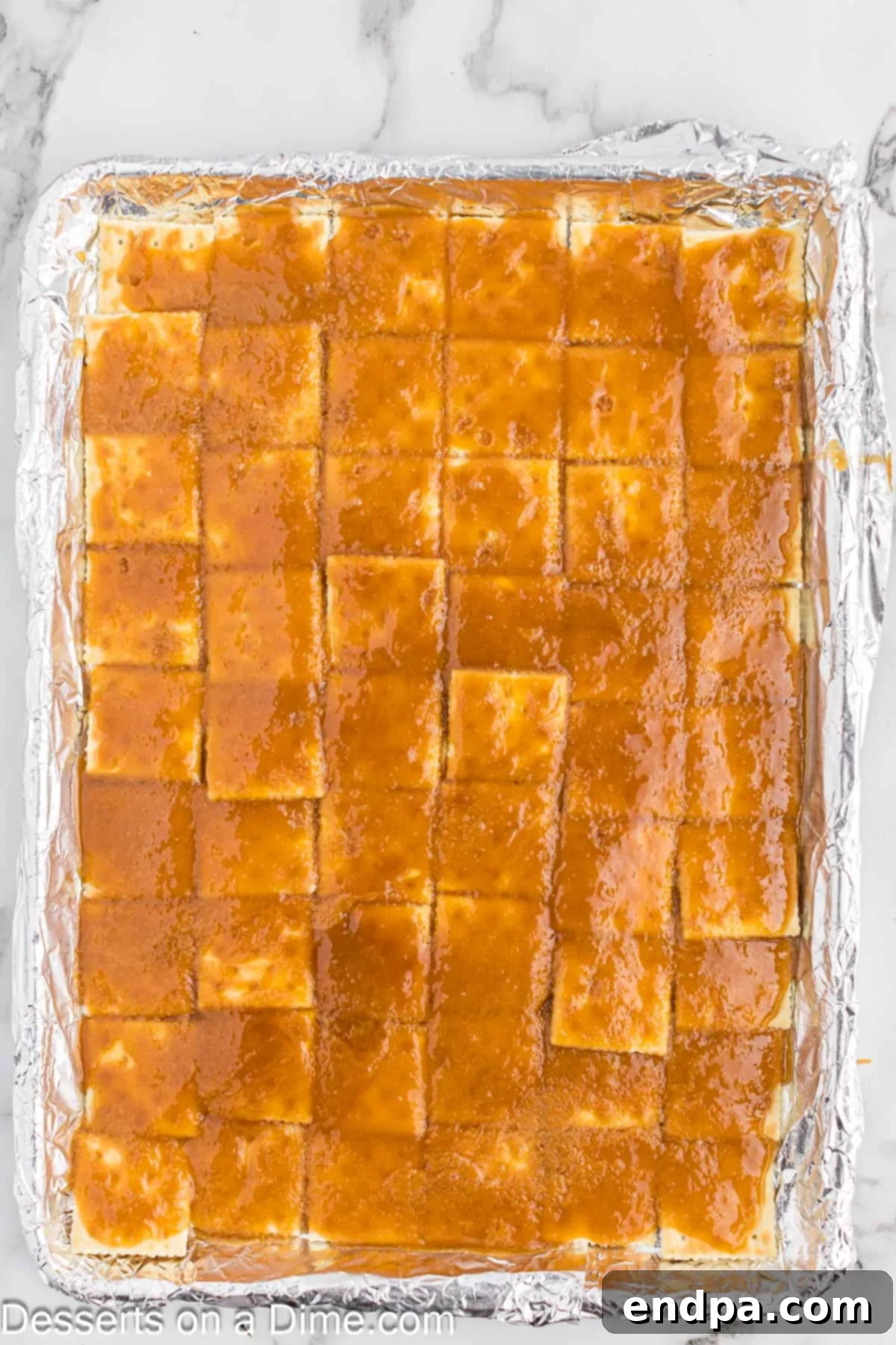 Saltine crackers thoroughly coated with the glistening brown sugar toffee mixture, ready for baking in the oven.