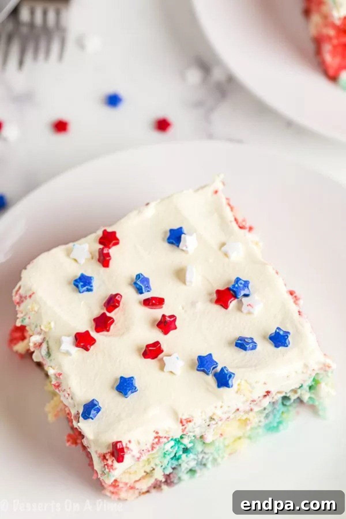 Close up image of a piece of Red White and Blue Poke Cake on a white plate, showcasing the colorful layers.
