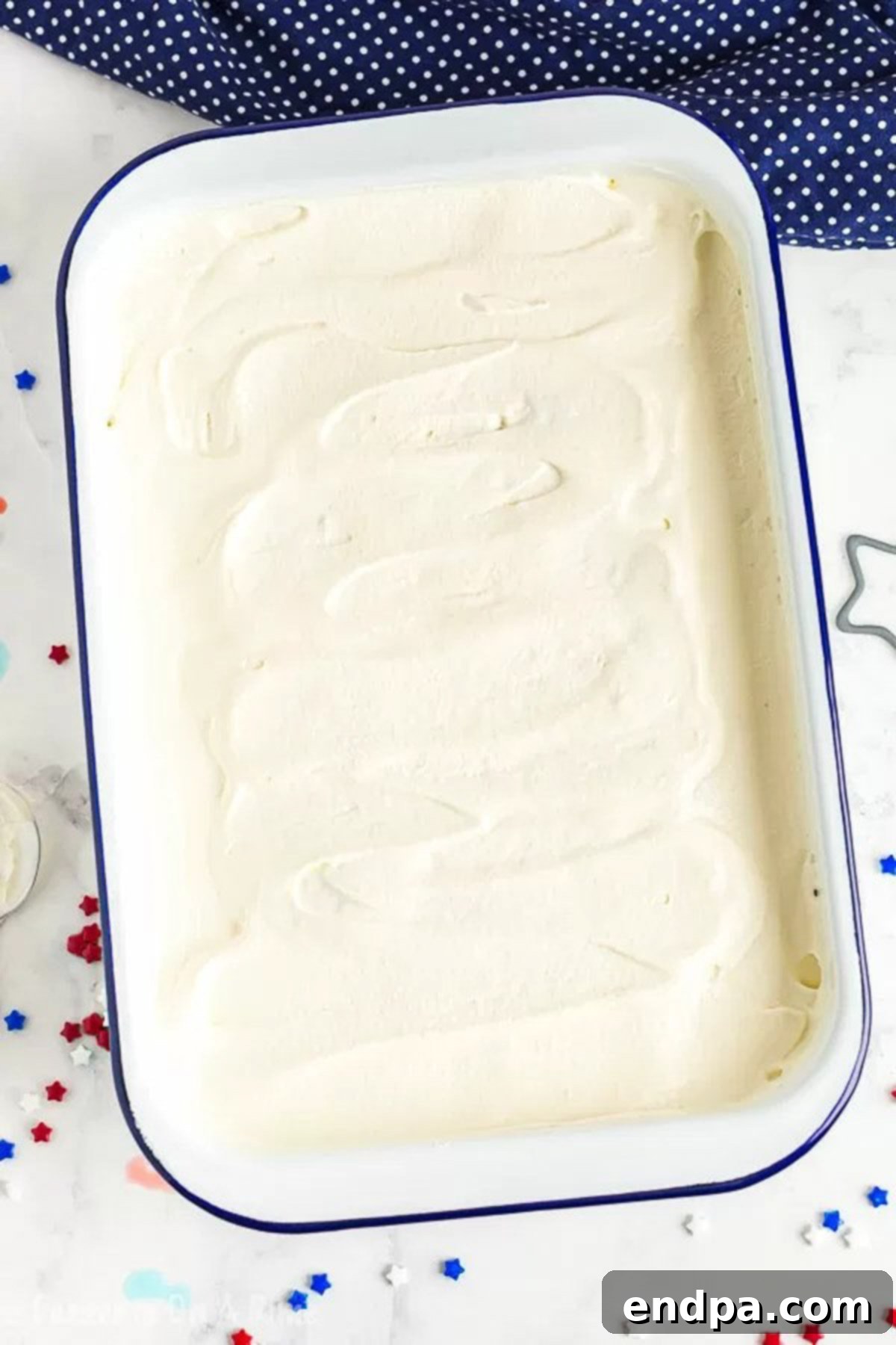Close up image of a frosted patriotic poke cake in a cake pan, topped with sprinkles.