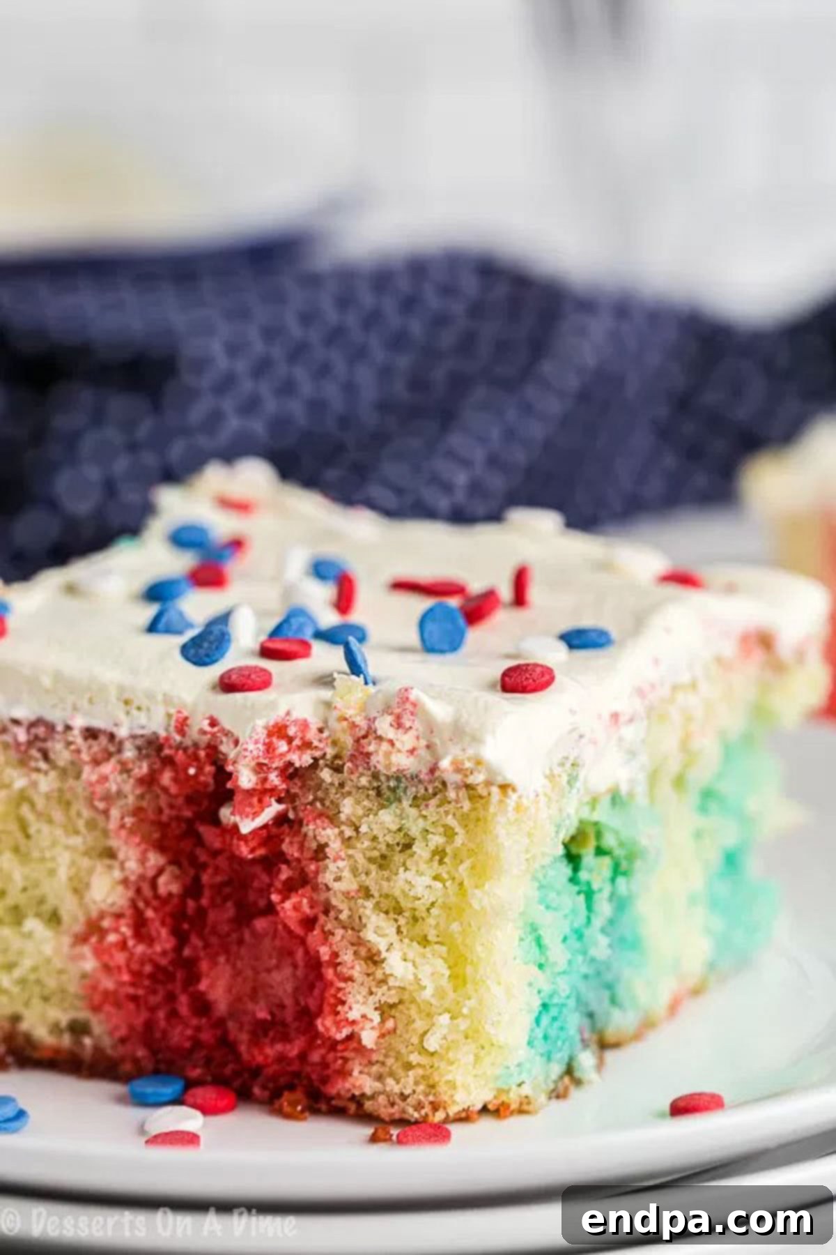 Close up image of a slice of patriotic poke cake on a white plate, showing the festive layers.