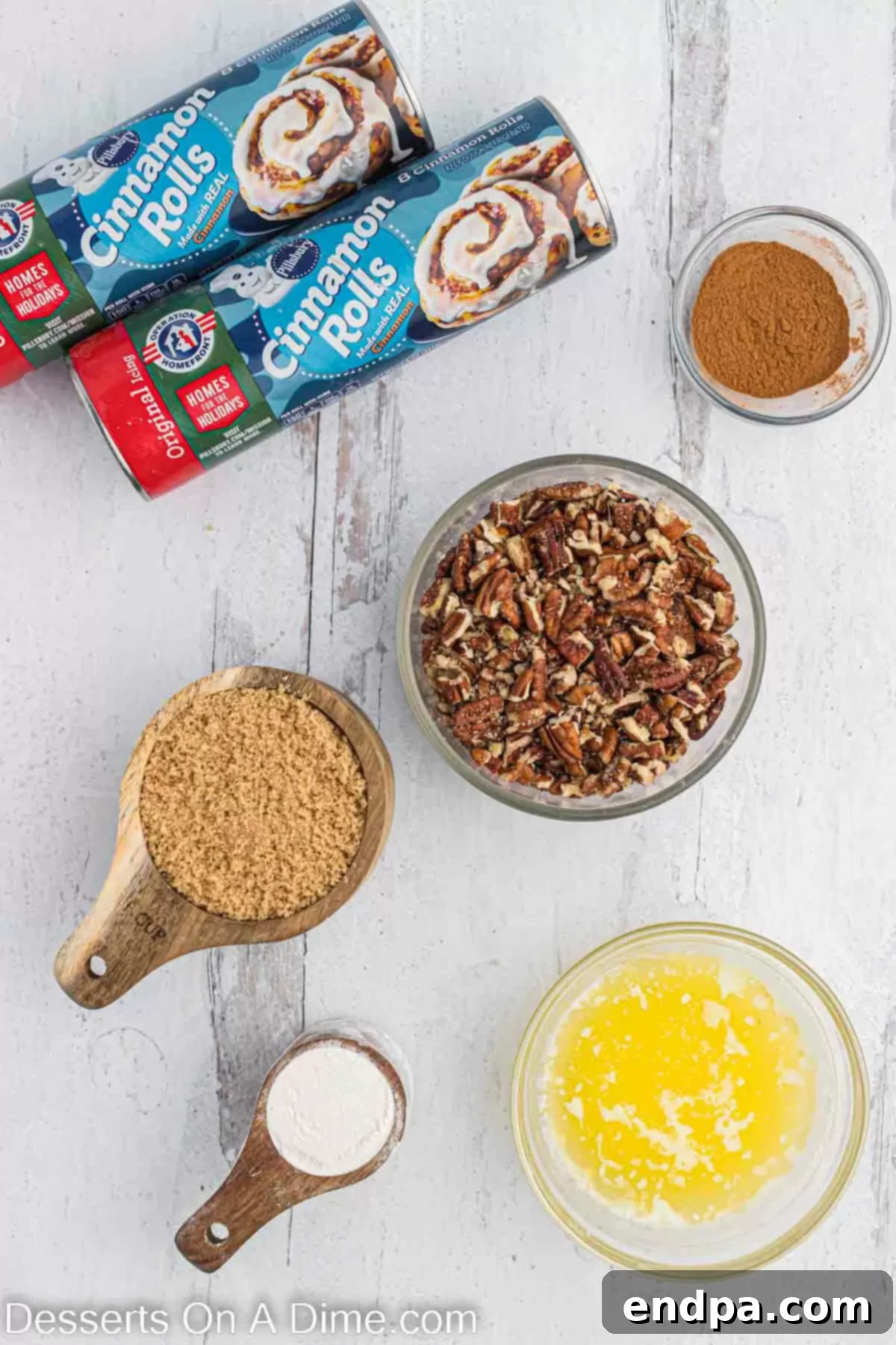 Homemade Cinnamon Roll Pie 3 A vibrant flat lay of all the essential ingredients for cinnamon roll pie: two cans of cinnamon rolls, a bowl of rich brown sugar, all-purpose flour, ground cinnamon, a stick of butter, and a mound of chopped pecans.