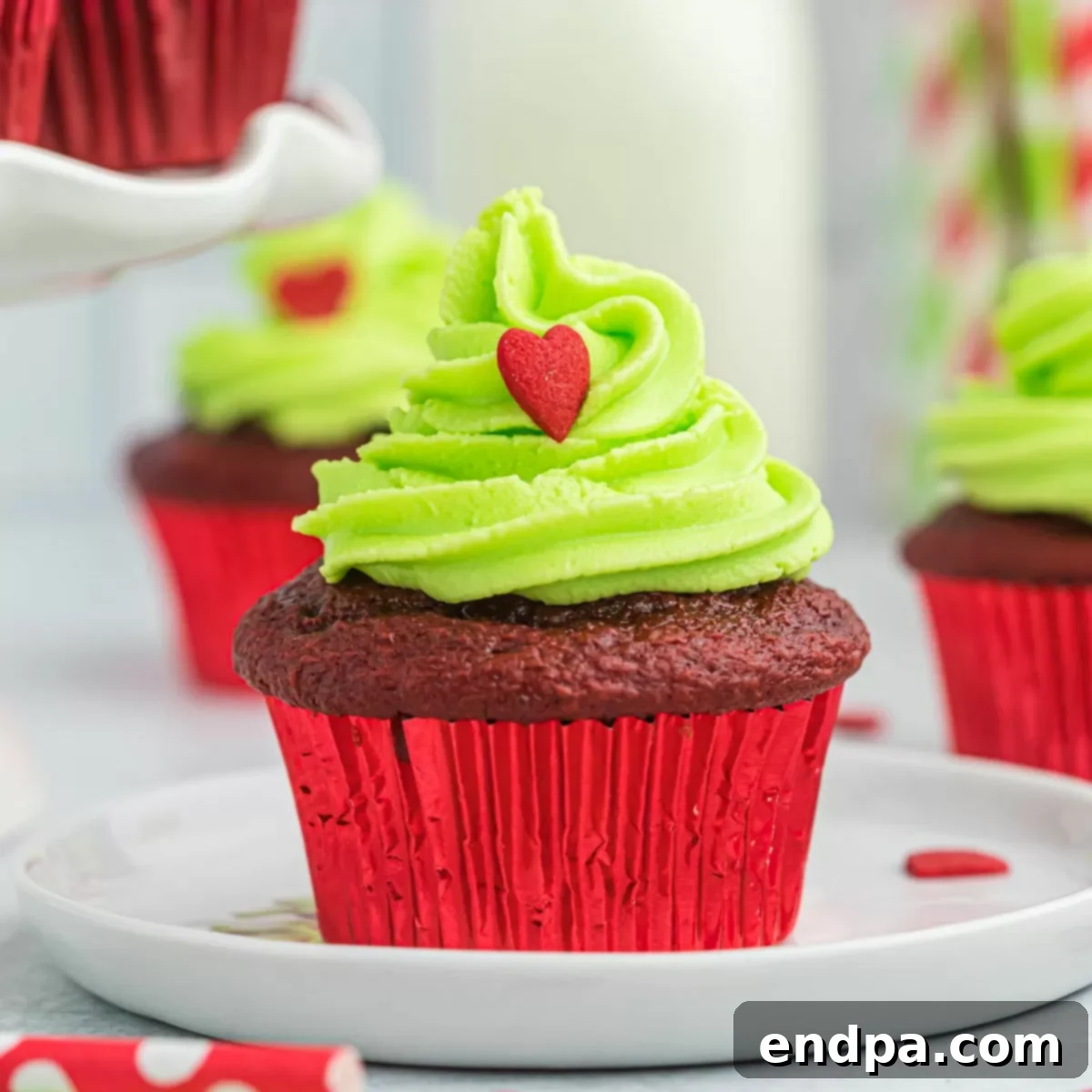 A square image displaying a perfectly frosted Grinch cupcake with green icing and a red heart sprinkle.