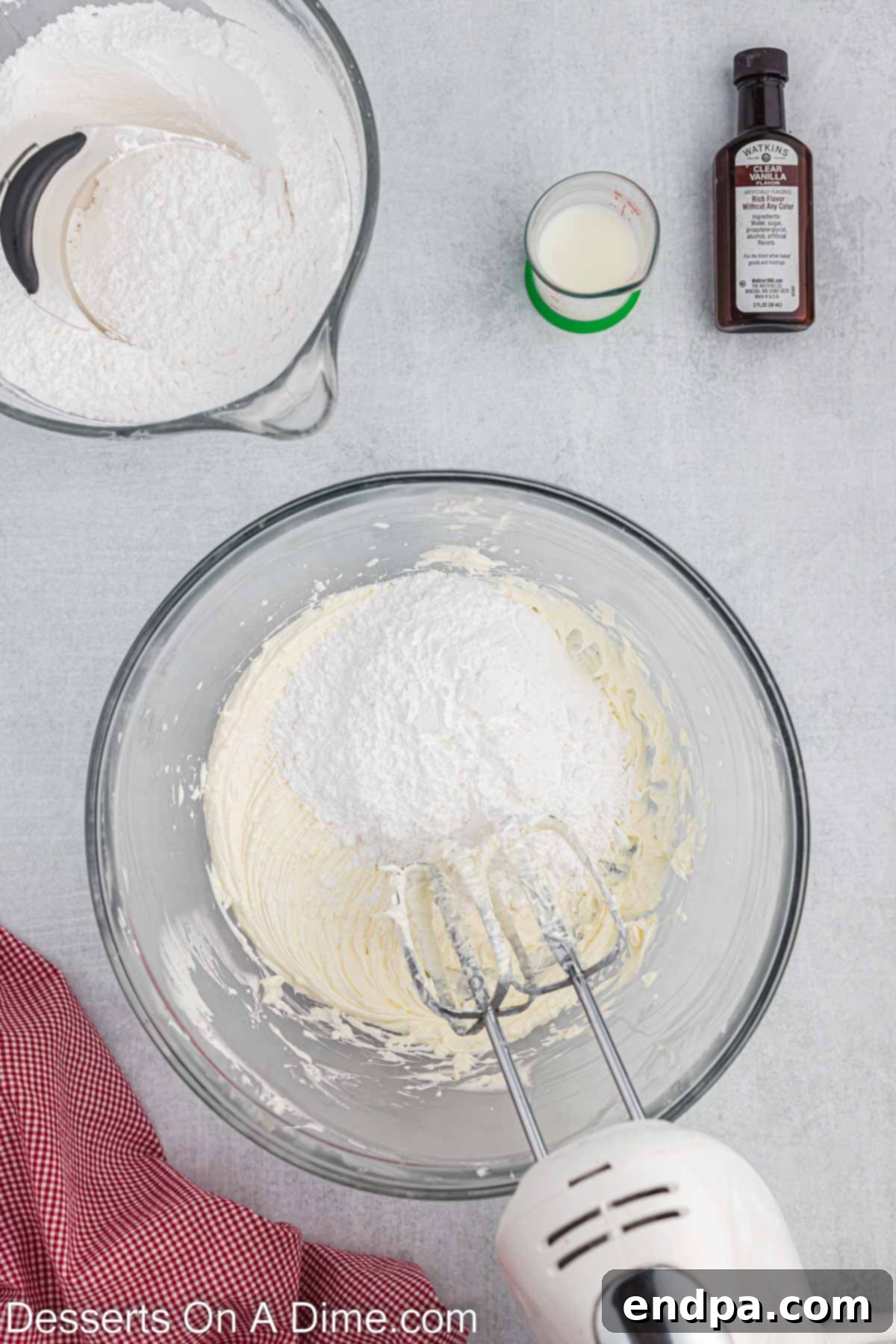 Powdered sugar being slowly and carefully added, one cup at a time, to the creamed butter and shortening mixture in a mixing bowl while the mixer is on low speed.