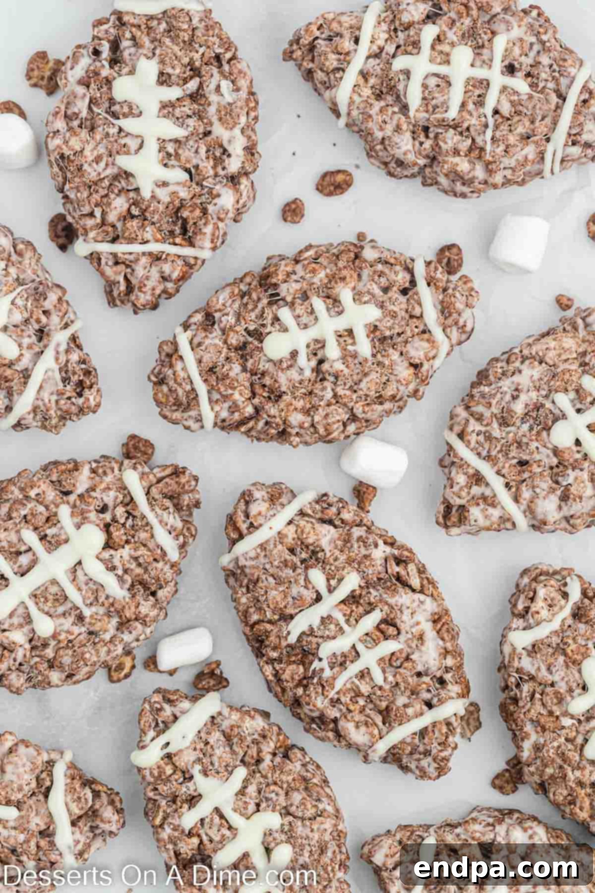 A collection of finished football-shaped Rice Krispie treats, beautifully decorated with white chocolate laces, spread out on a flat surface.