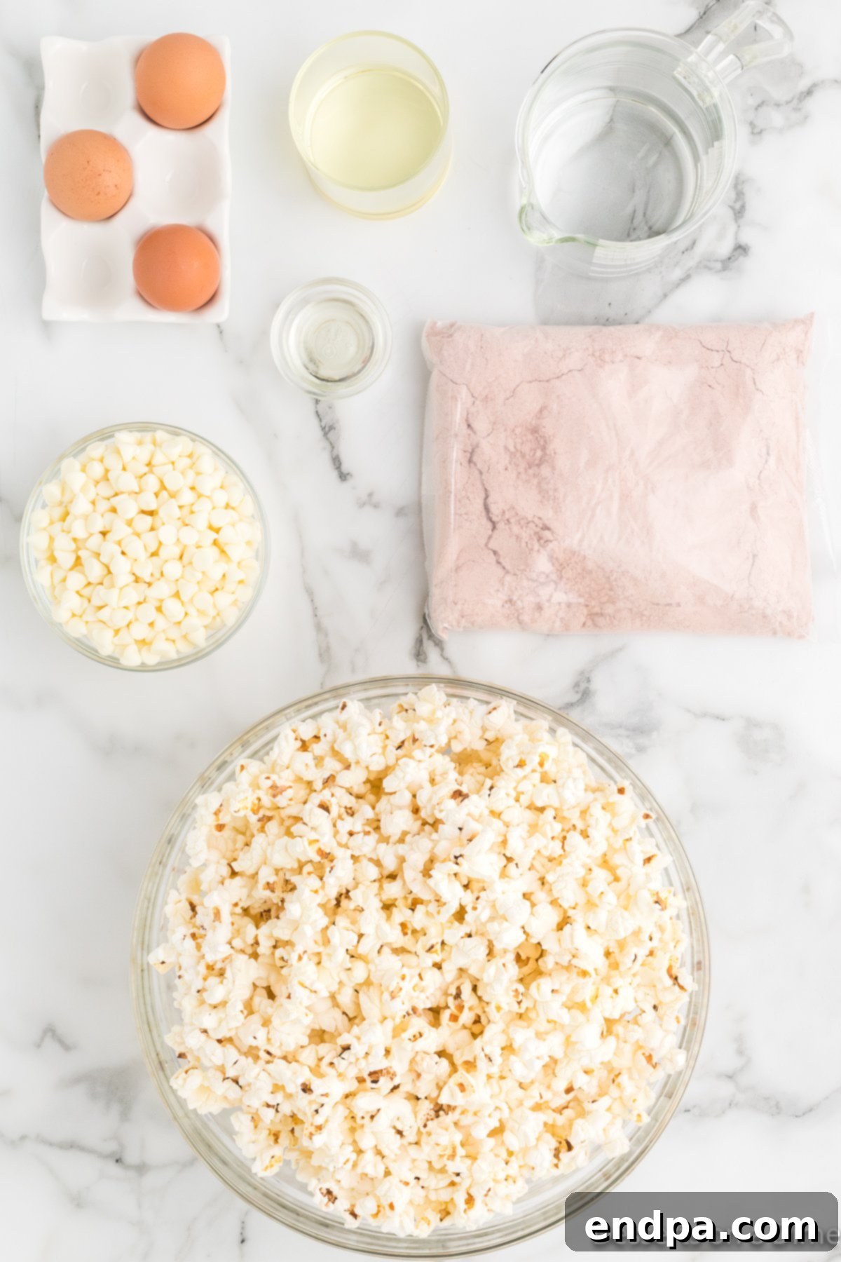Layout of ingredients for Red Velvet Popcorn: bowls of popped popcorn, red velvet cake mix, white chocolate chips, and a bottle of vegetable oil.