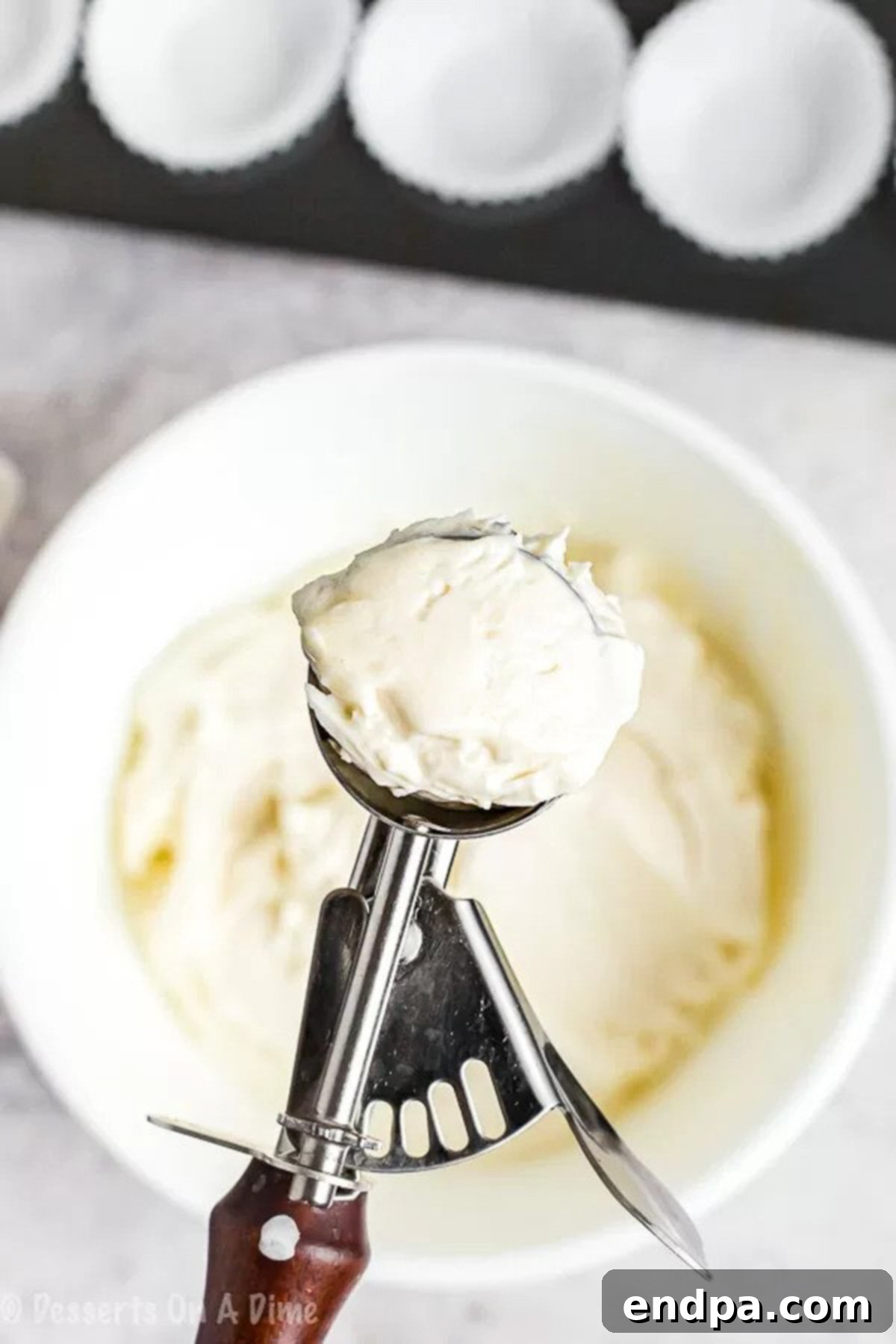 Keto Fat Bomb batter being scooped onto a cookie scoop, showing a precise portion ready to be transferred into a muffin pan, for uniform shaping.