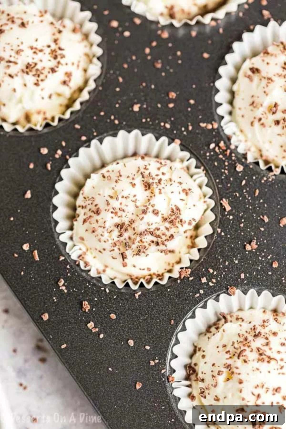 A mini muffin pan completely filled with Keto Cheesecake Fat Bombs, already topped with delicate chocolate shavings, sitting ready for the chilling process.