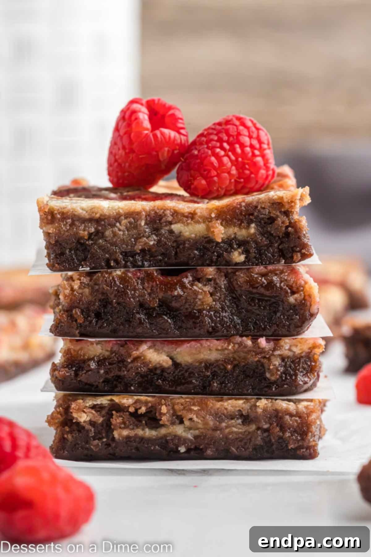 Raspberry Brownies stacked with parchment paper in between with fresh raspberries on the top