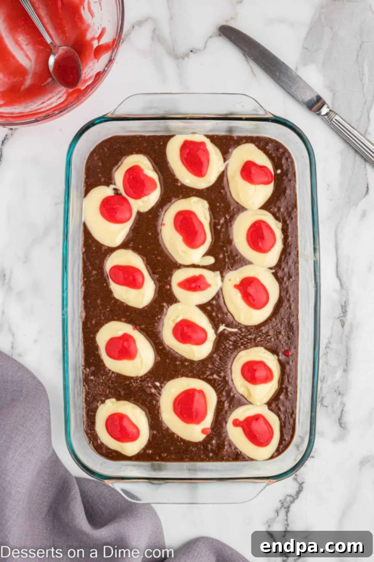 Dropping cheesecake layer on brownie batter and topping with raspberries