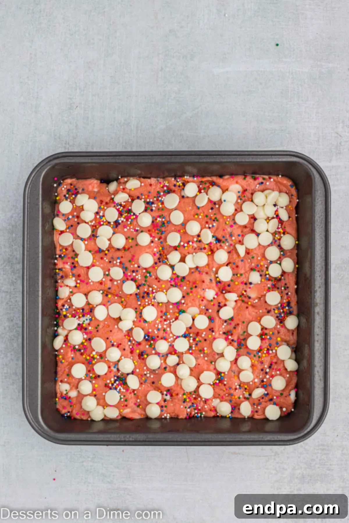 The unbaked strawberry brownie batter in the pan, topped with the remaining white chocolate chips and sprinkles.