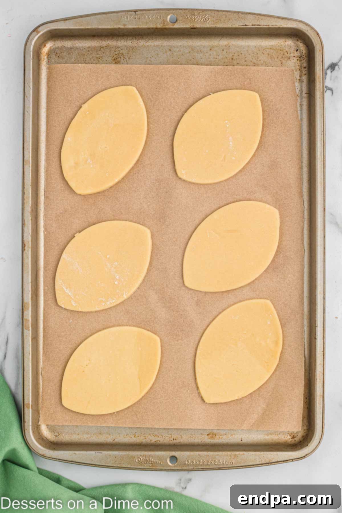 Touchdown Sugar Cookies 10 Football-shaped sugar cookies carefully placed on a baking sheet lined with parchment paper, ready for the oven.